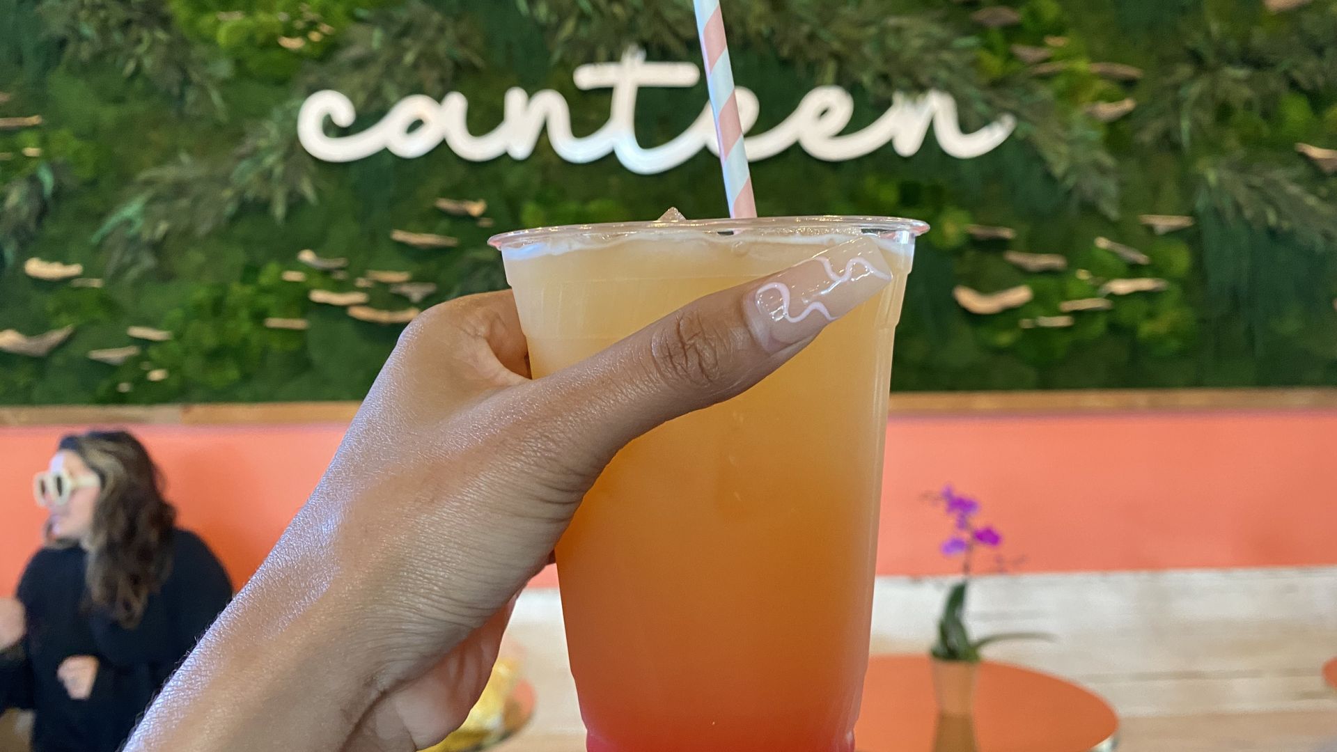 Hand holding a cocktail in front of neon signs that reads "Canteen"