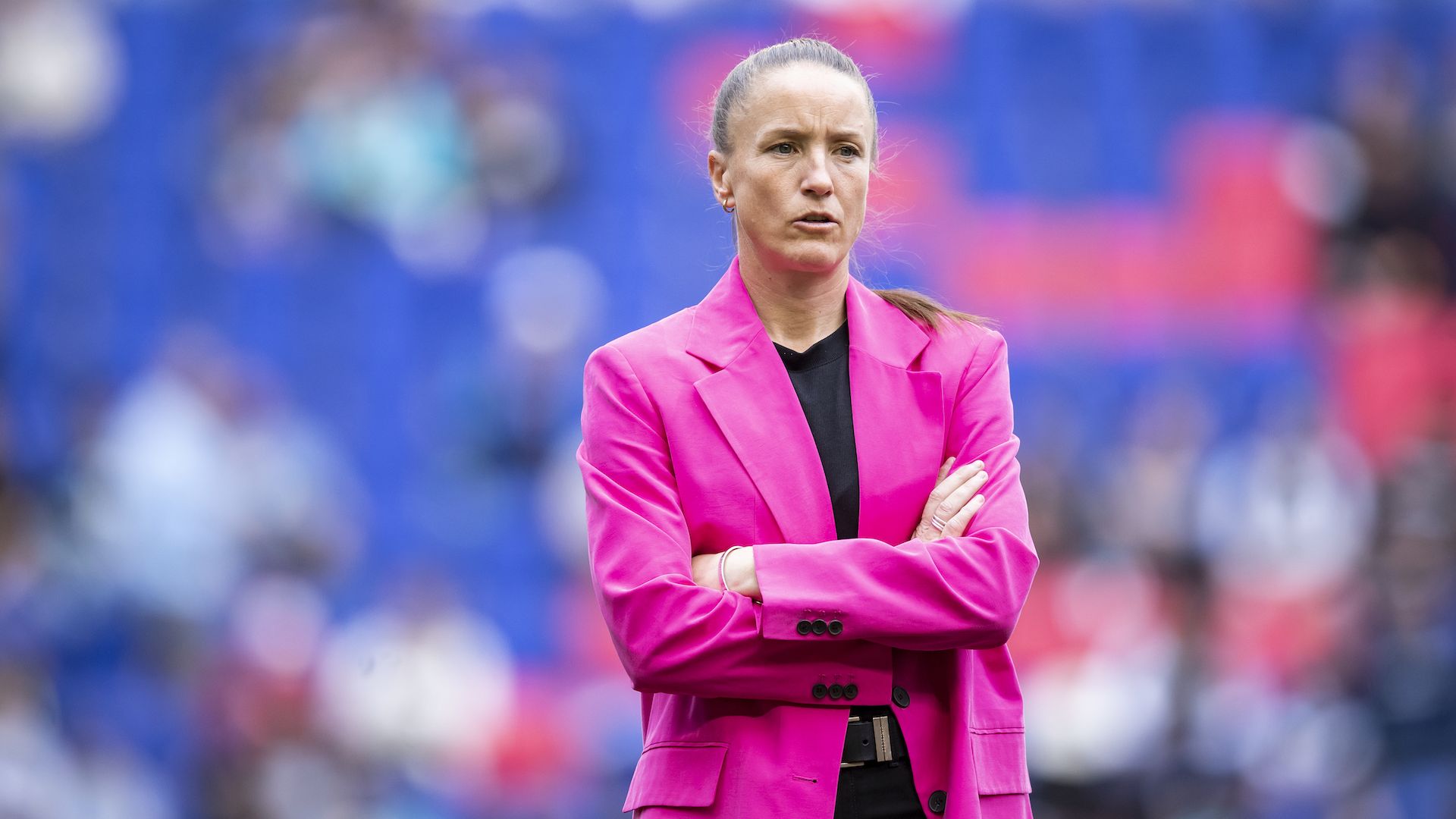 San Diego Wave coach Casey Stoney stands with her arms crossed wearing a pink blazer.
