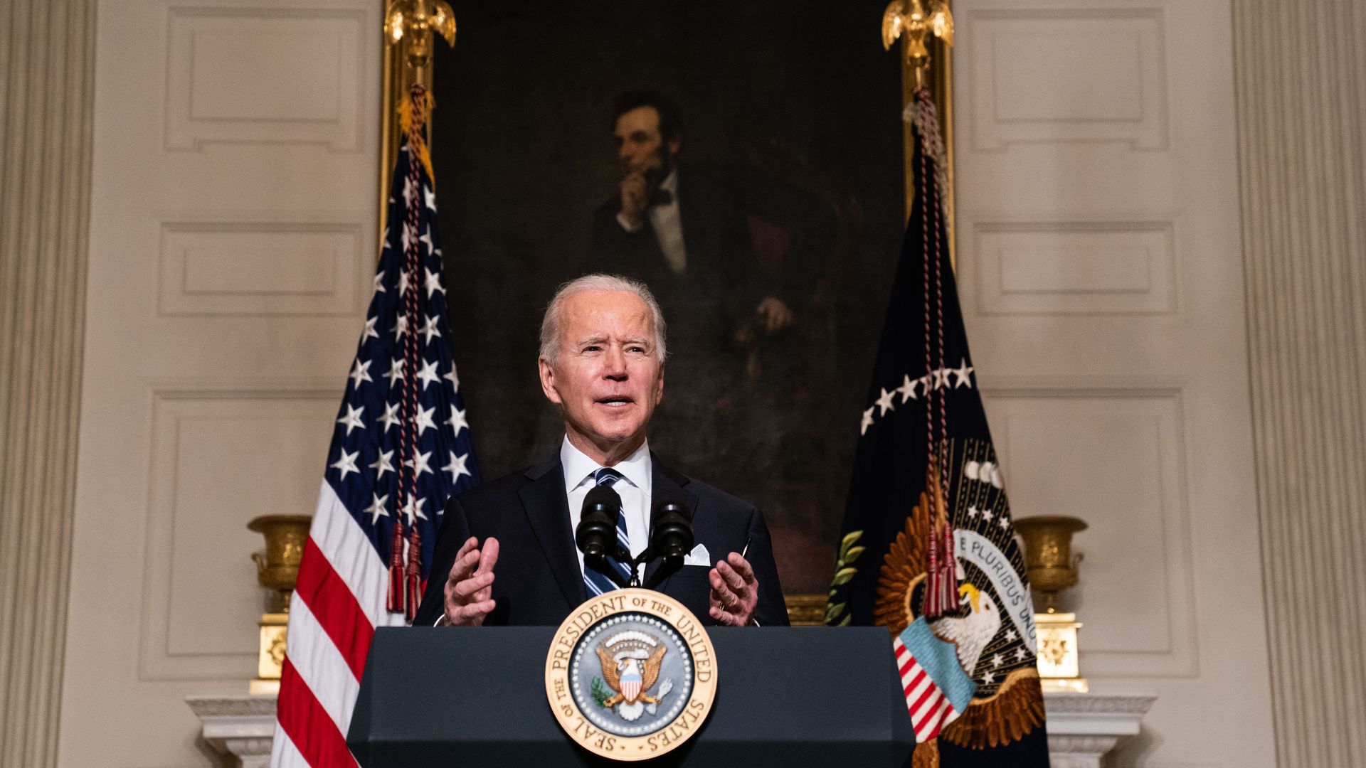 President Biden is seen speaking at the White House beneath a portrait of Abraham Lincoln.