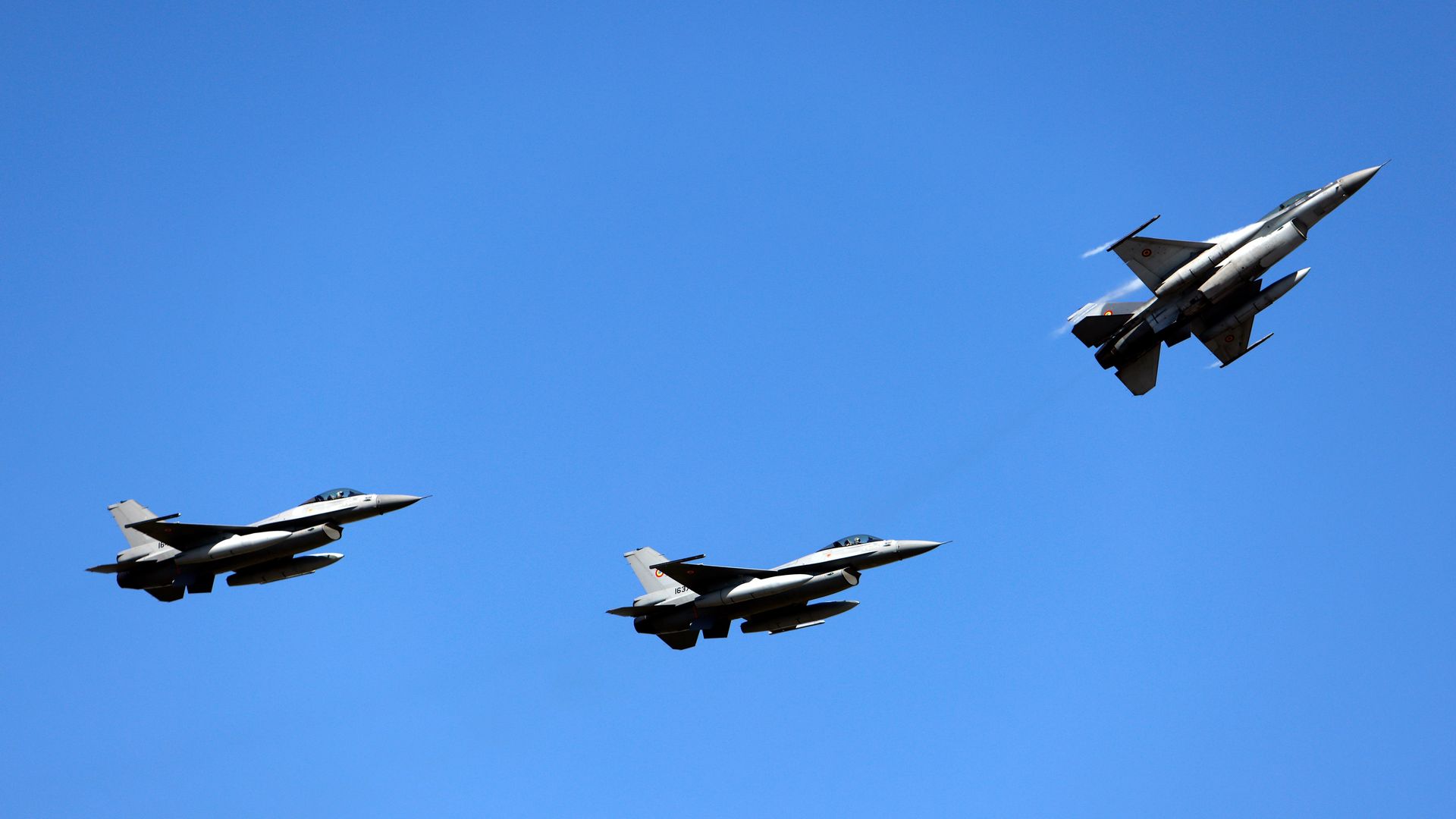 Three gray F-16 military jets fly in formation in a blue sky.