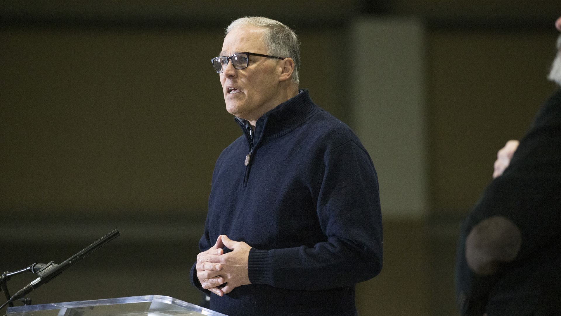 Photo of Jay Inslee speaking behind a podium with his hands folded in front of him