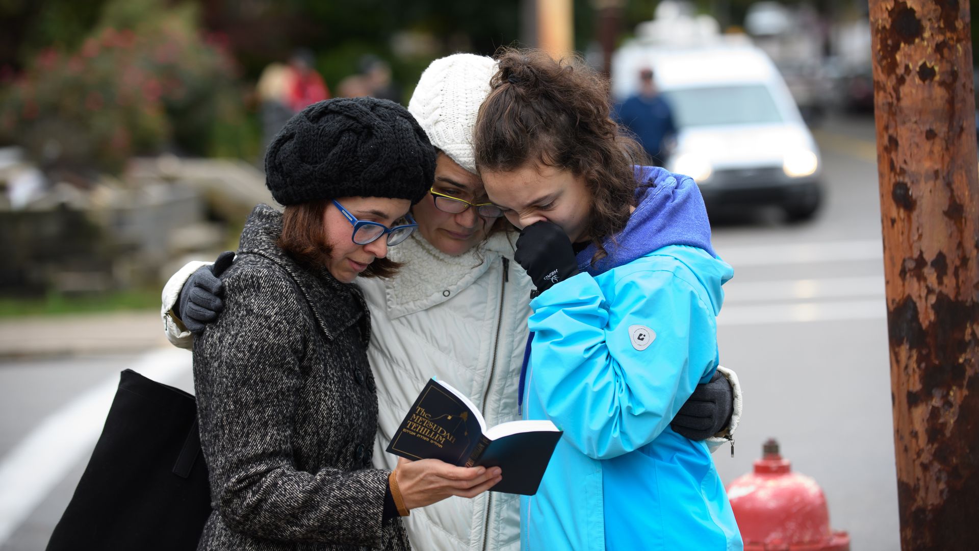 Three women praying from a prayer book at the shooting scene.