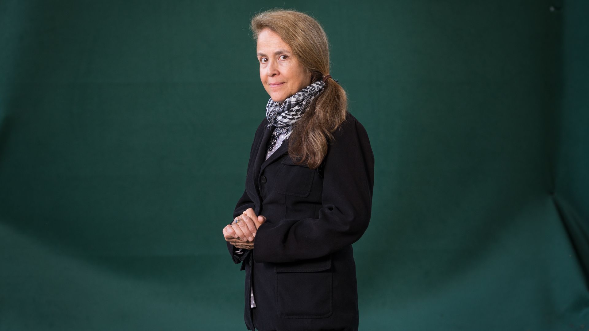 Naomi Shihab Nye poses in front of a dark green backdrop.