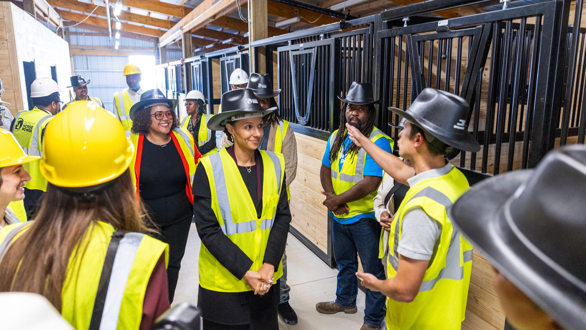 A group in hard cowboy hats tours under construction stables