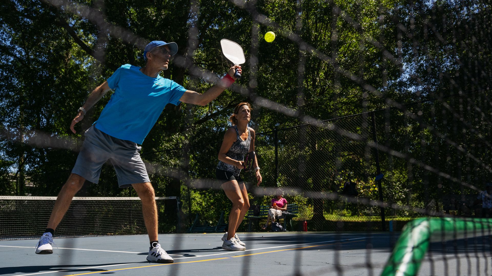 Pickleball players hit a ball across a court net.
