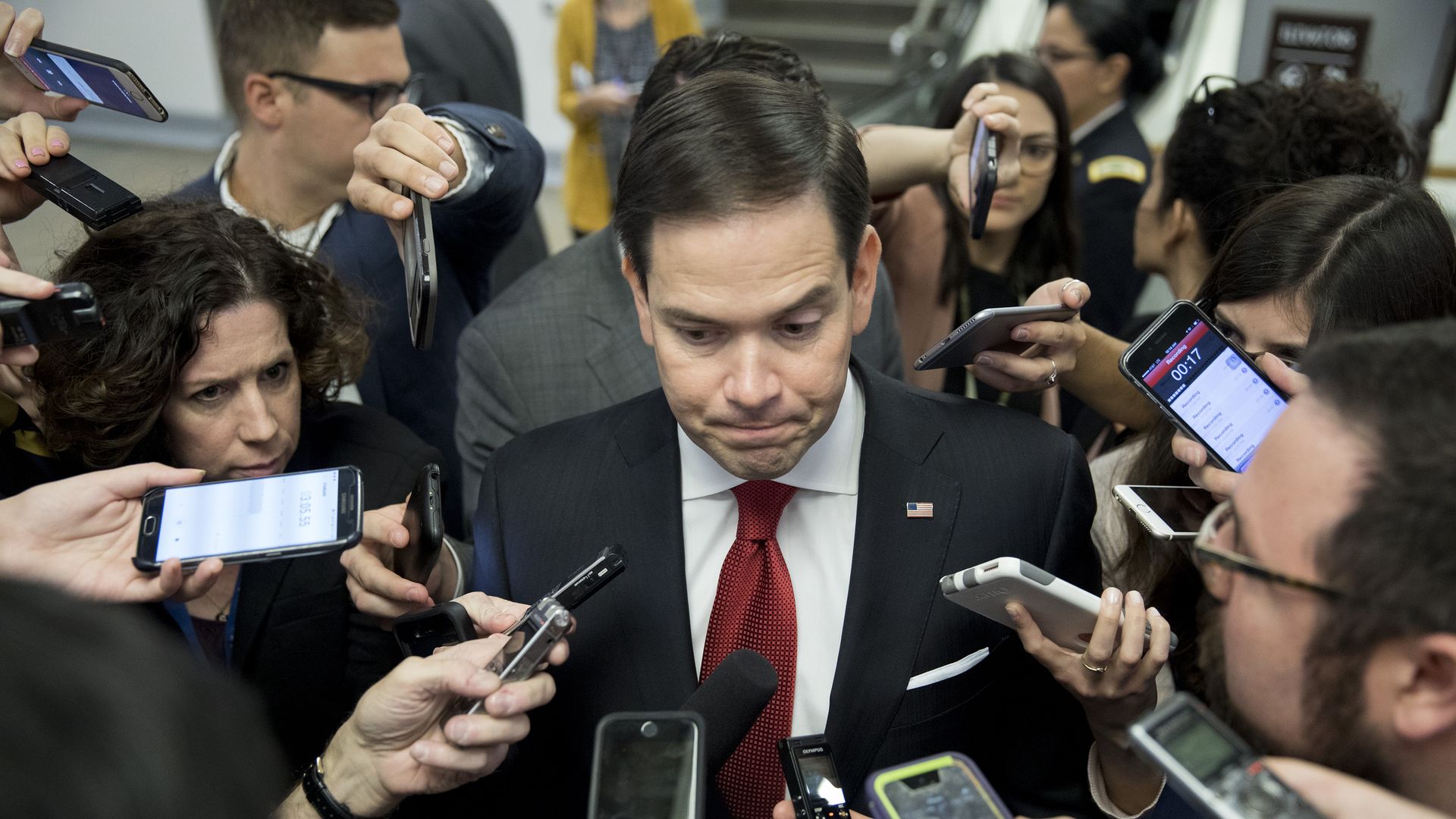 Marco Rubio looks stern surrounded by reporters and microphones