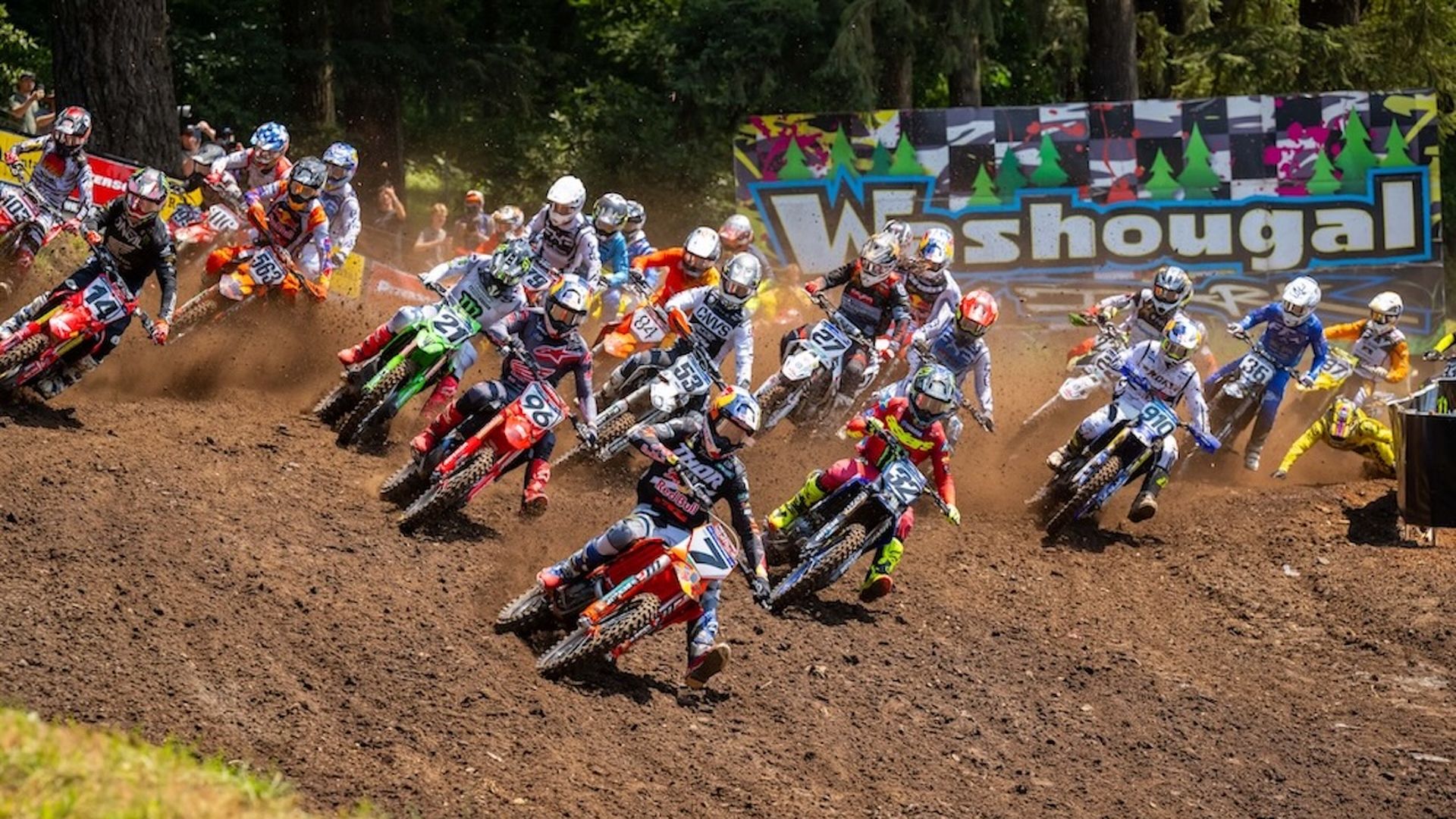 A photo of dozens of motorsports riders on bikes traversing a dirt hill with a sign that says "Washougal" on it behind them.