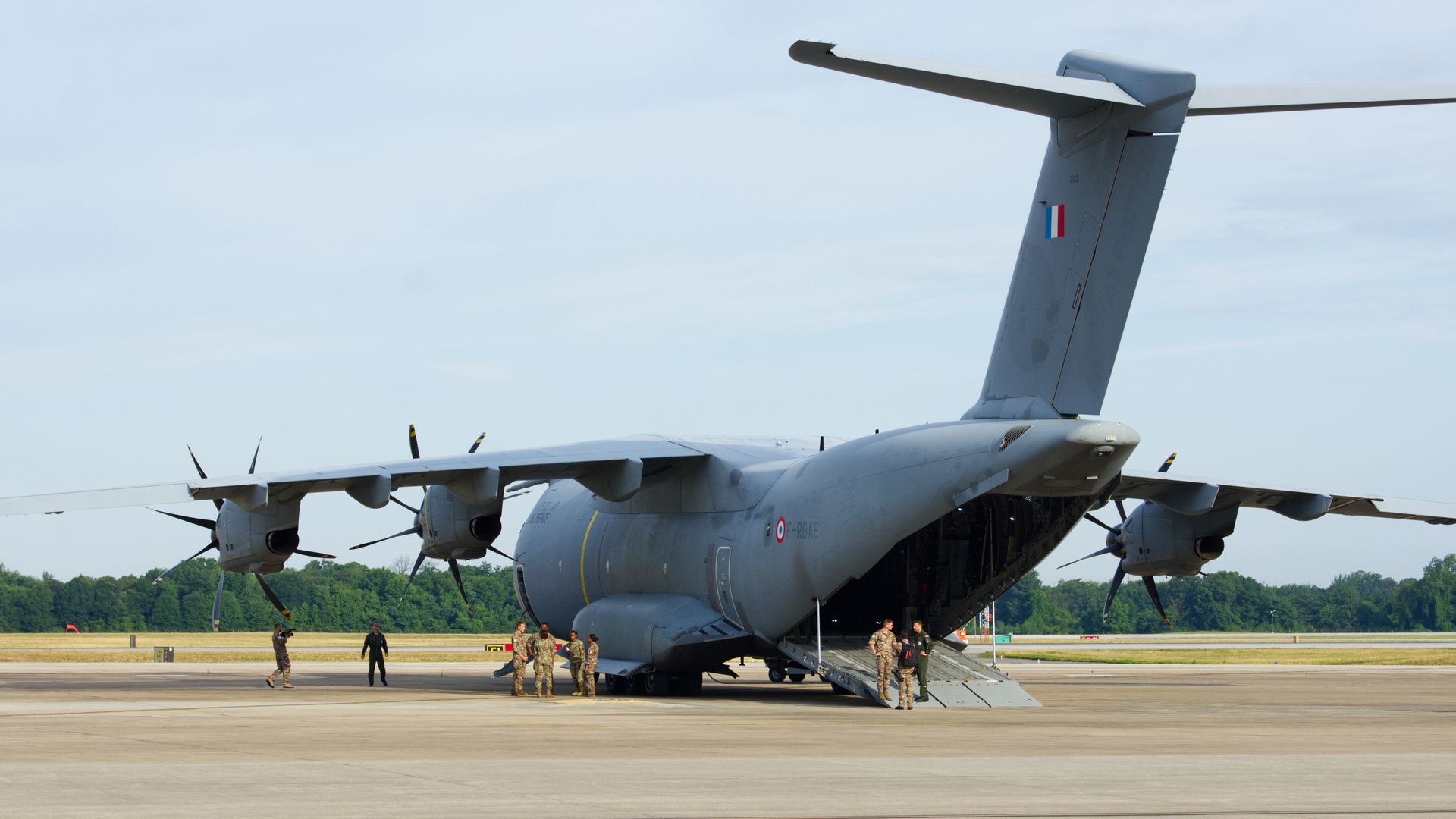 Rear view of a gray French Air Force A400M on a runway, cargo ramp lowered.