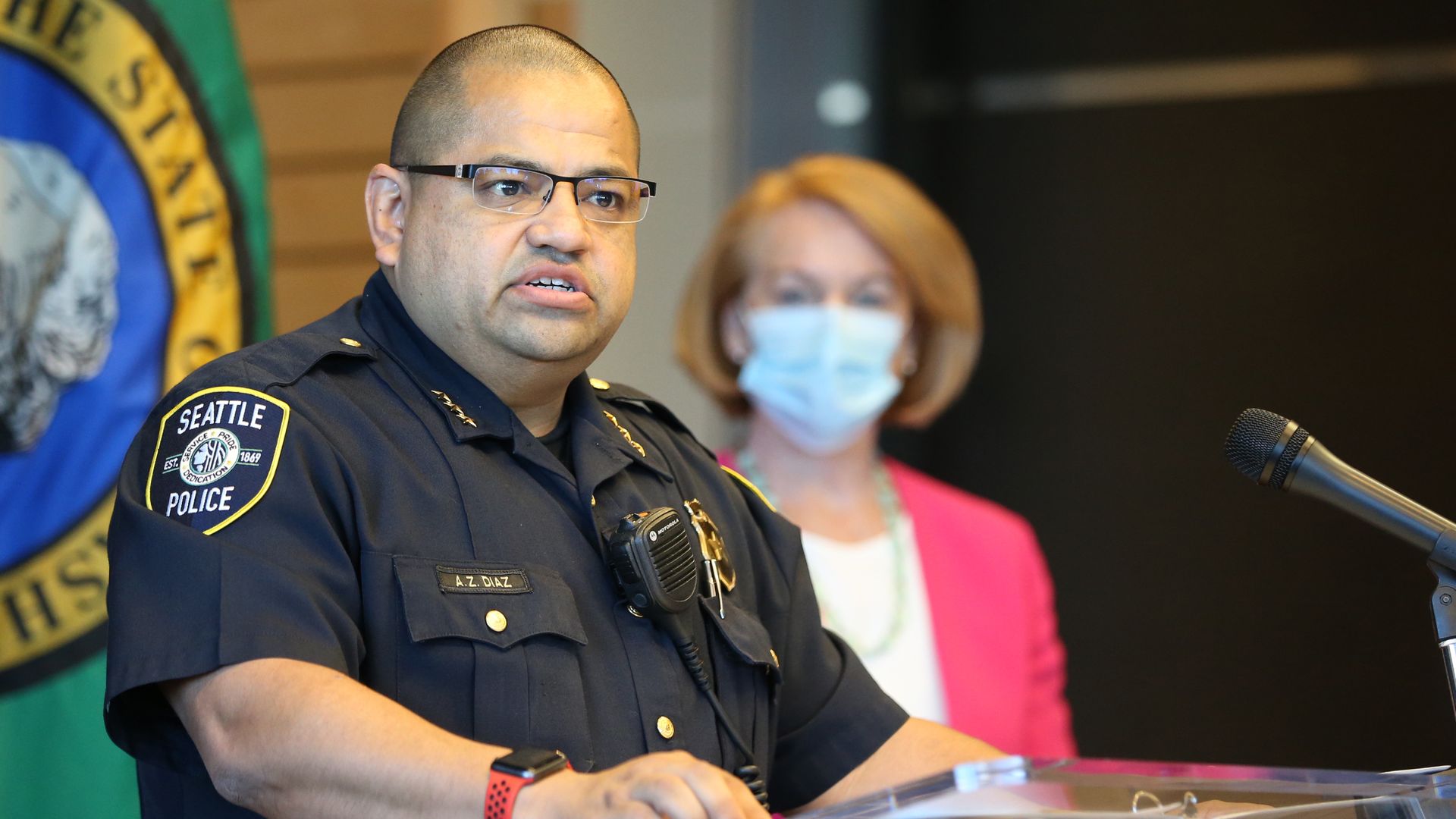 A police leader in a short-sleeved uniform shirt speaks at a podium. 