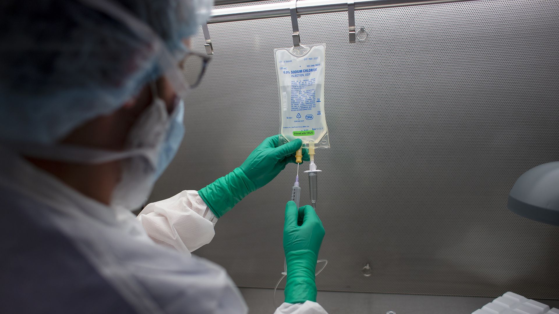 Photo of a health care worker in scrubs and gloves holding an IV bag and needle