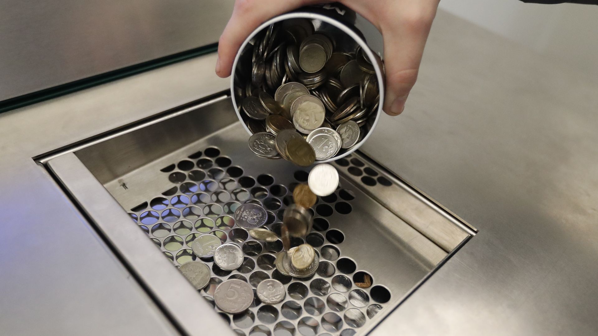 A photo of coins being poured from a cup into a coin machine.