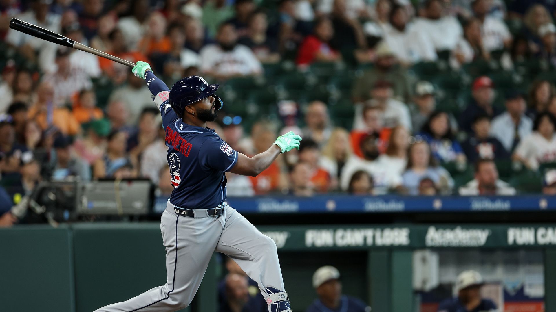 Junior Caminero #13 of the Tampa Bay Rays hits a home run in the first inning against the Houston Astros. He's shown here watching the ball leave his bat, and wearing gray pants and a dark blue shirt.