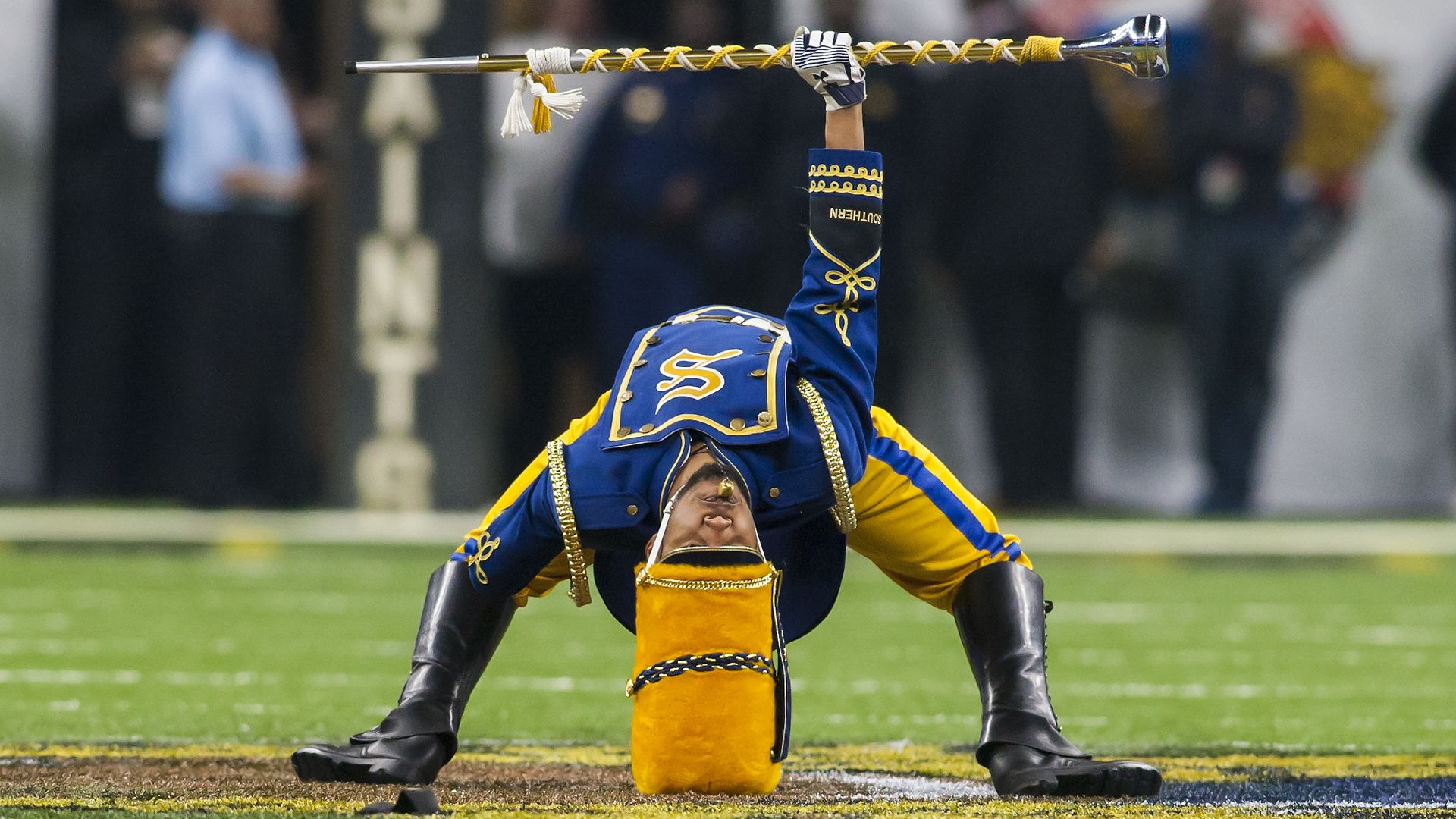 A drum major leans backwards all the way so his hat rests on the ground behind him.