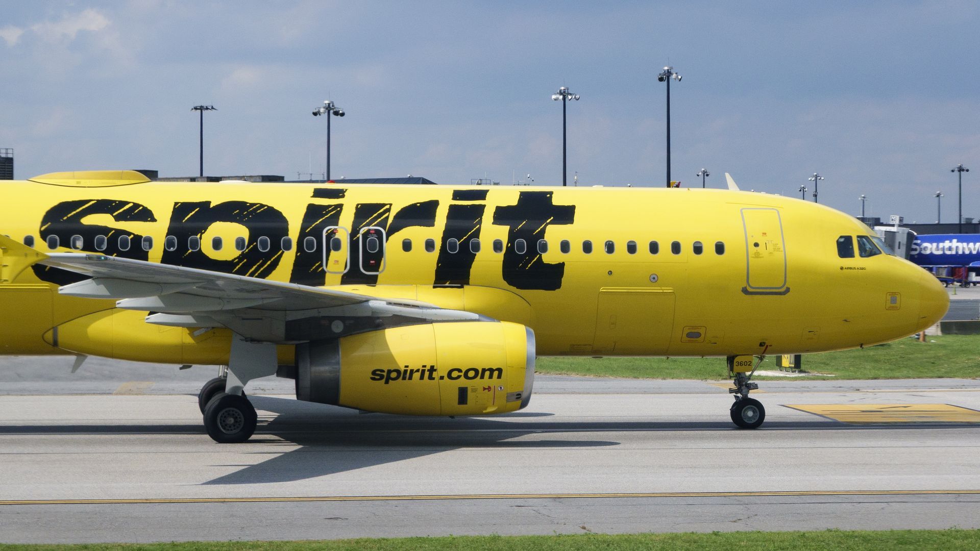 Yellow Spirit Airlines airplane with black lettering on runway, clear sky, and airport lights in the background.