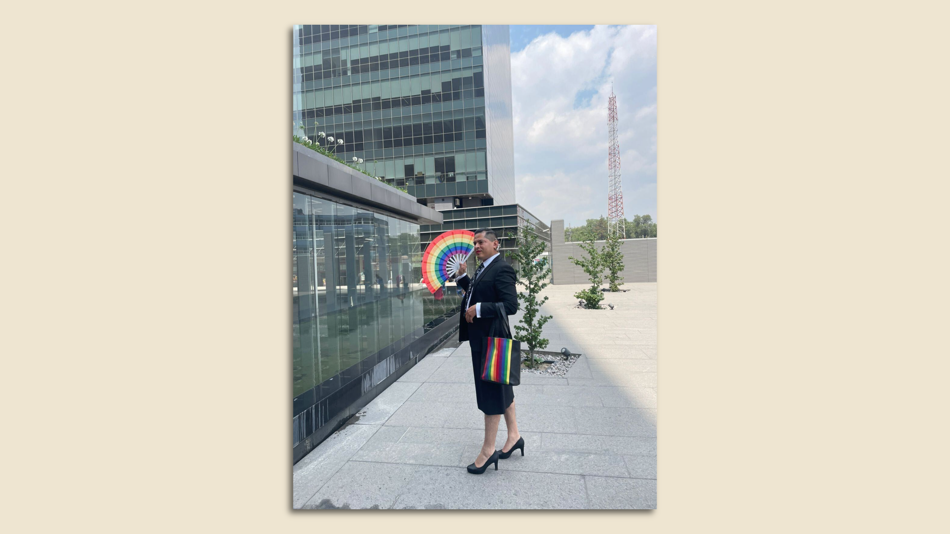 Ociel Baena of Mexico City stands outside holding a bag with a rainbow and a fan with rainbow colors 