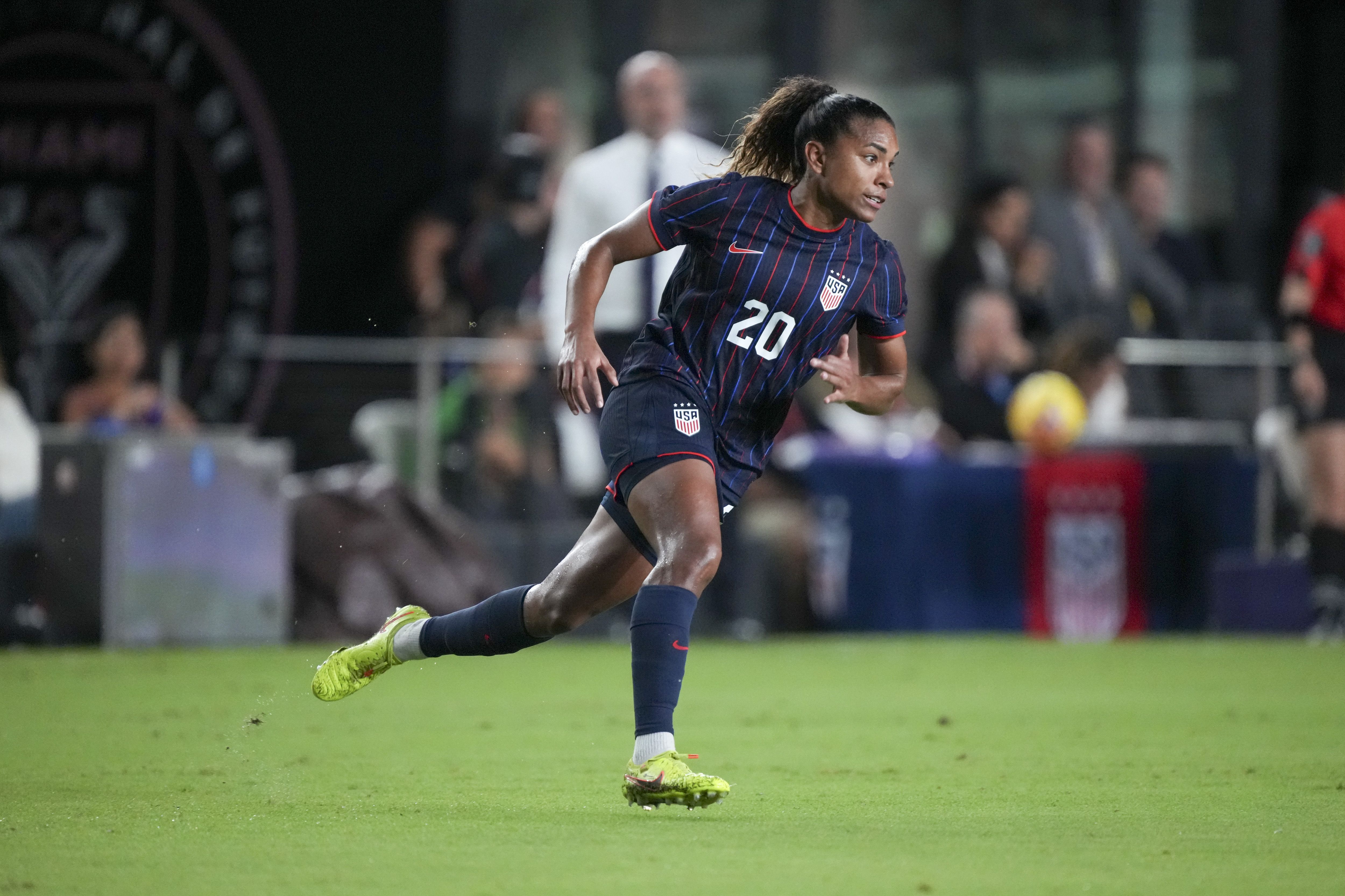 Catarina Macario in a dark blue striped #20 U.S. jersey runs on the soccer field after scoring a goal.