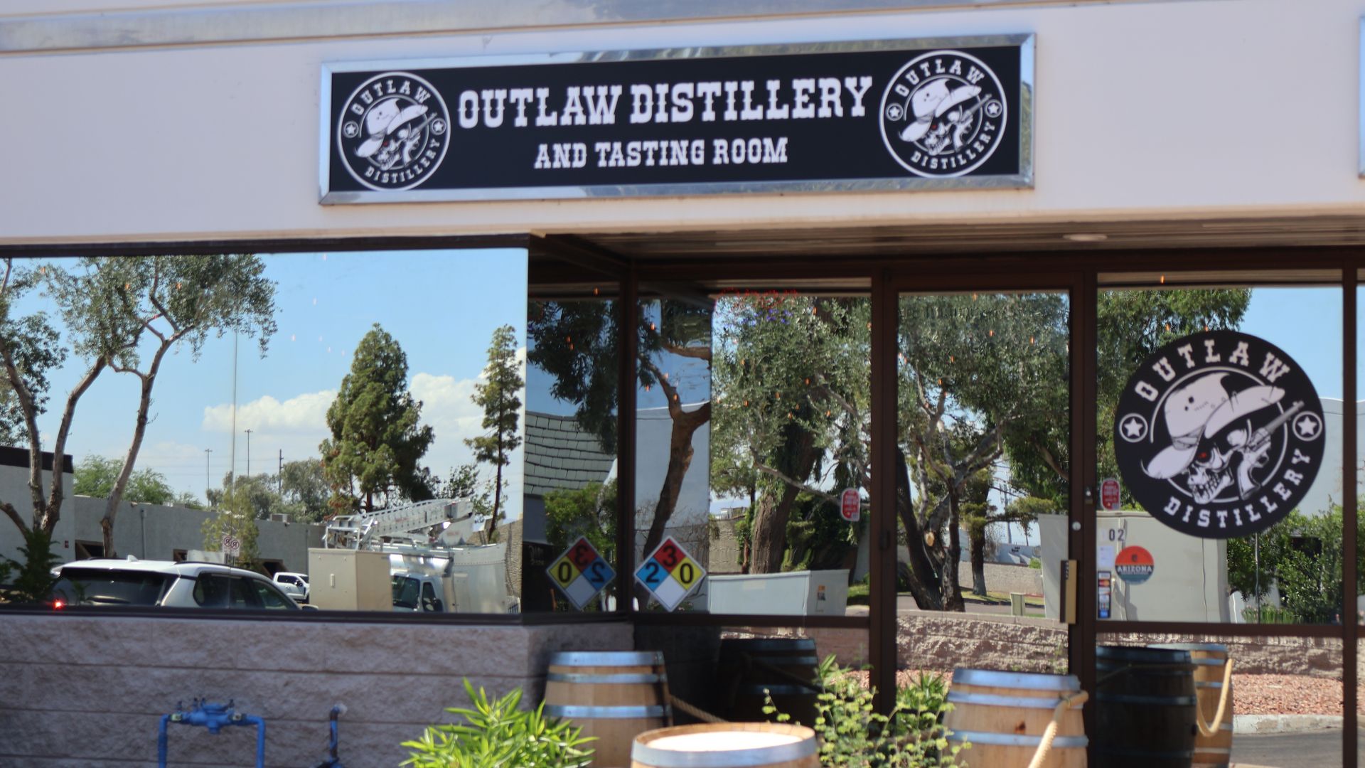 A storefront with mirrored windows, with a sign on the window and above the door for Outlaw Distillery.