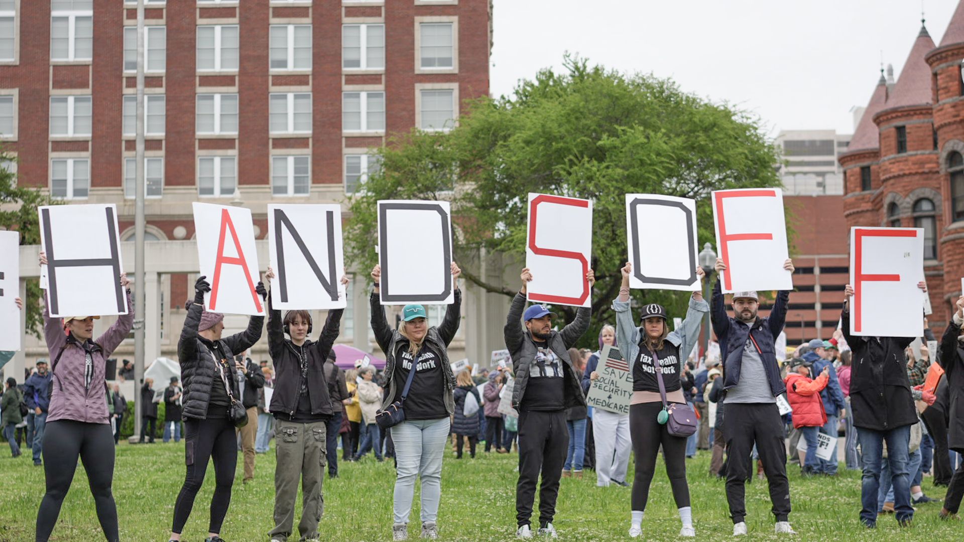people hold up signs that spell out Hands Off at a protest in downtown Dallas