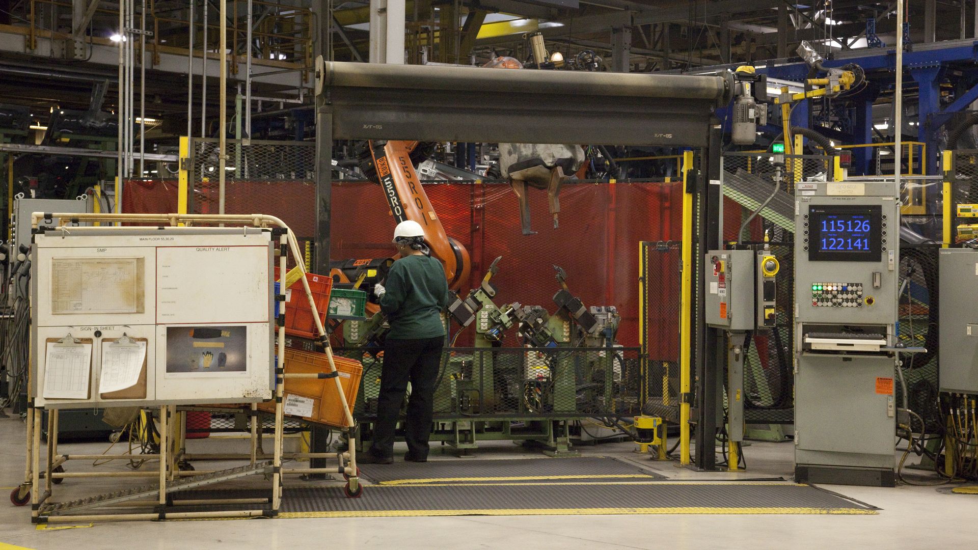 A worker in a green uniform stands a machine in a factory