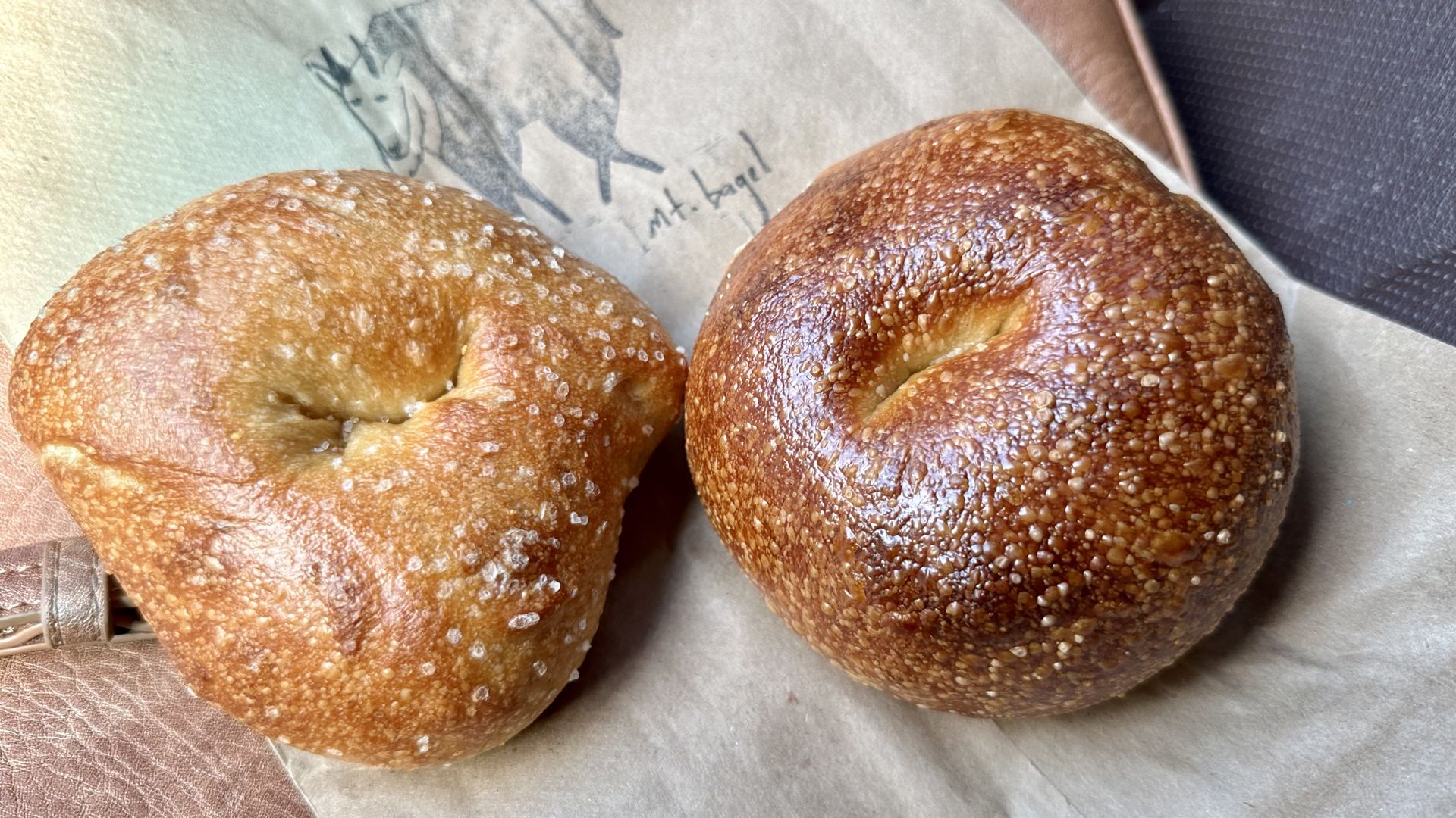 Two bagels side by side on a paper bag.