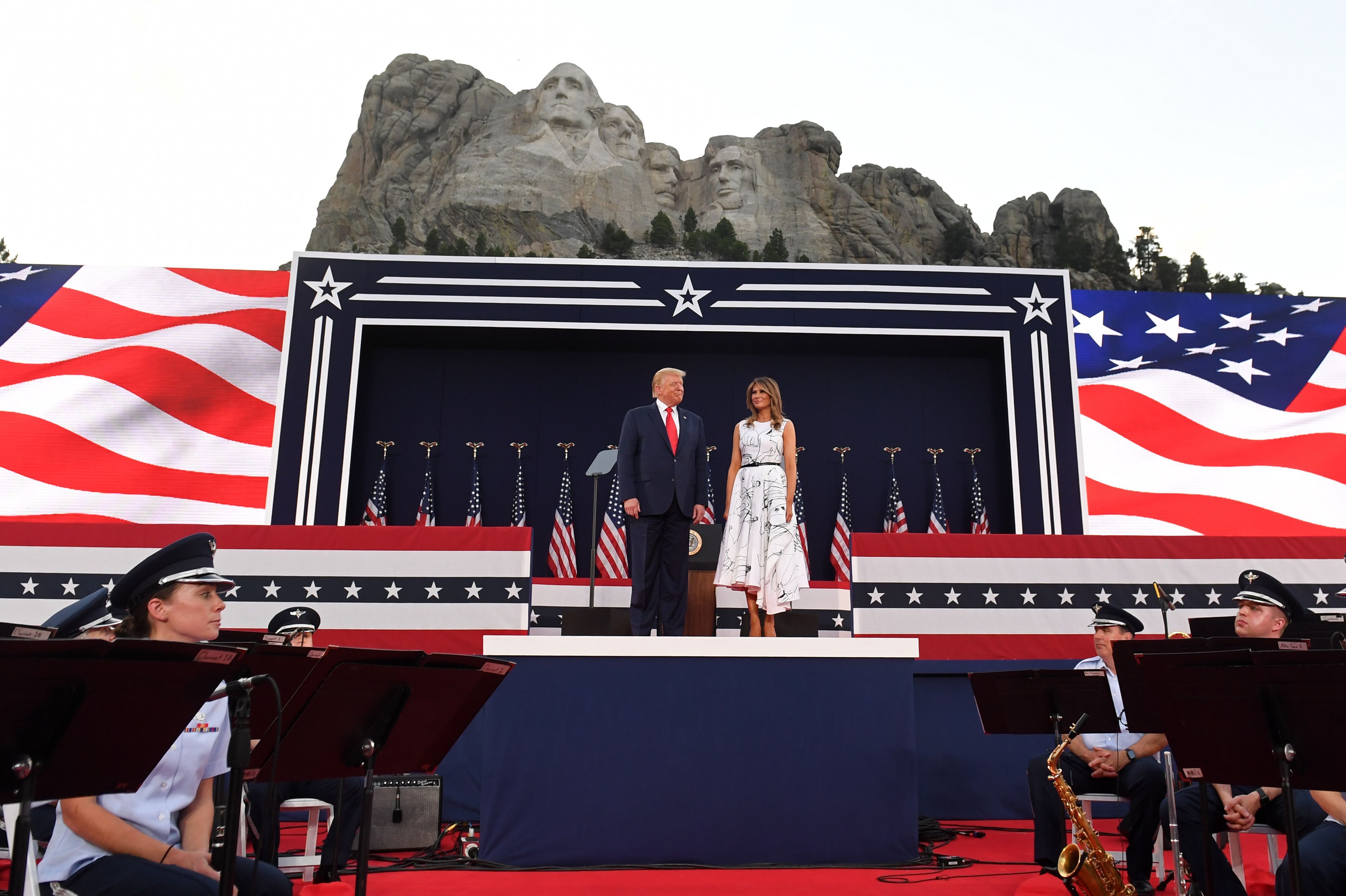 President Donald Trump and First Lady Melania Trump stand in front of Mount Rushmore on a stage
