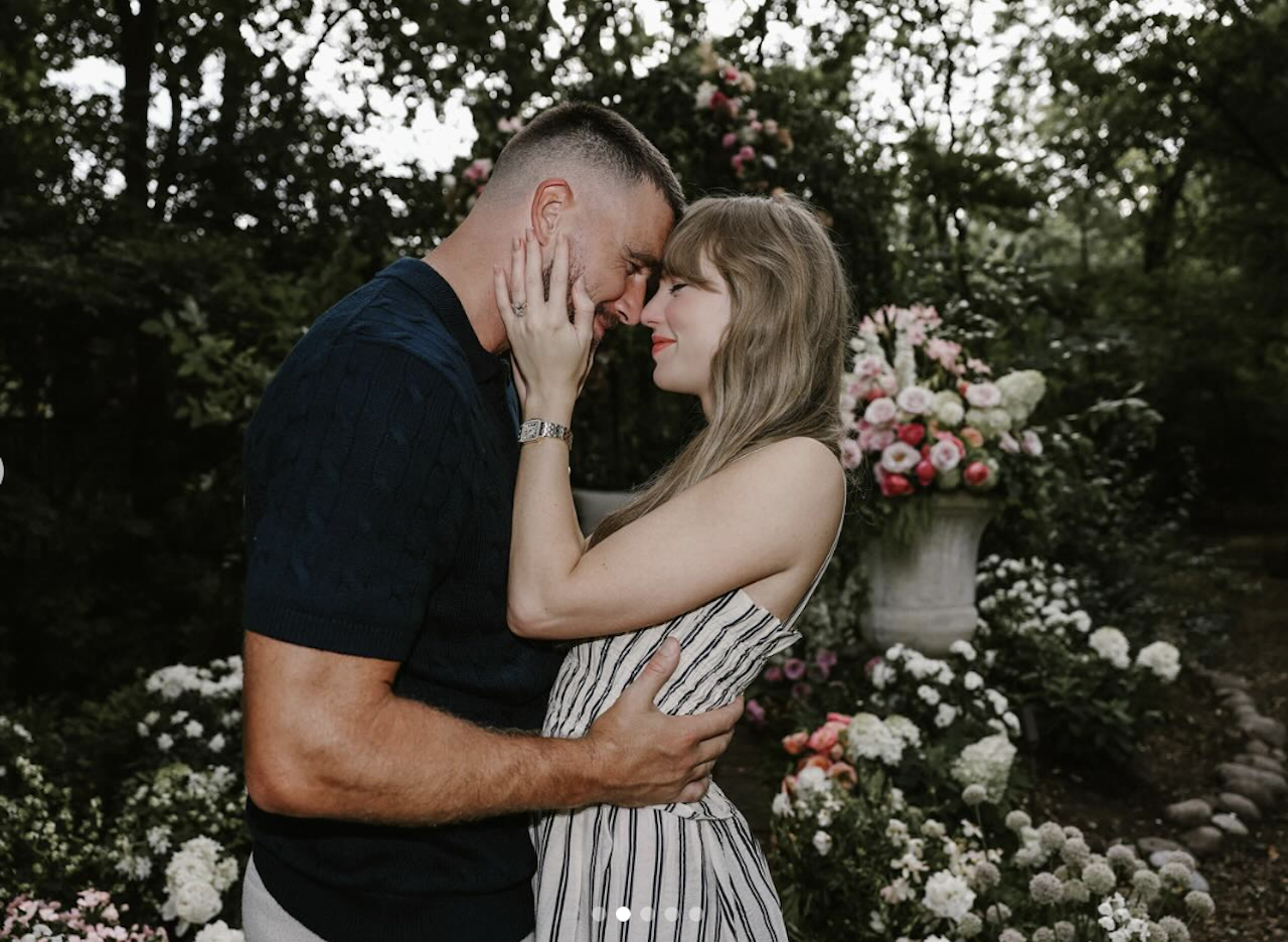 Couple embracing closely in a garden with abundant white and pink flowers, the woman in a striped dress and the man in a dark shirt, sharing an intimate moment with foreheads touching.