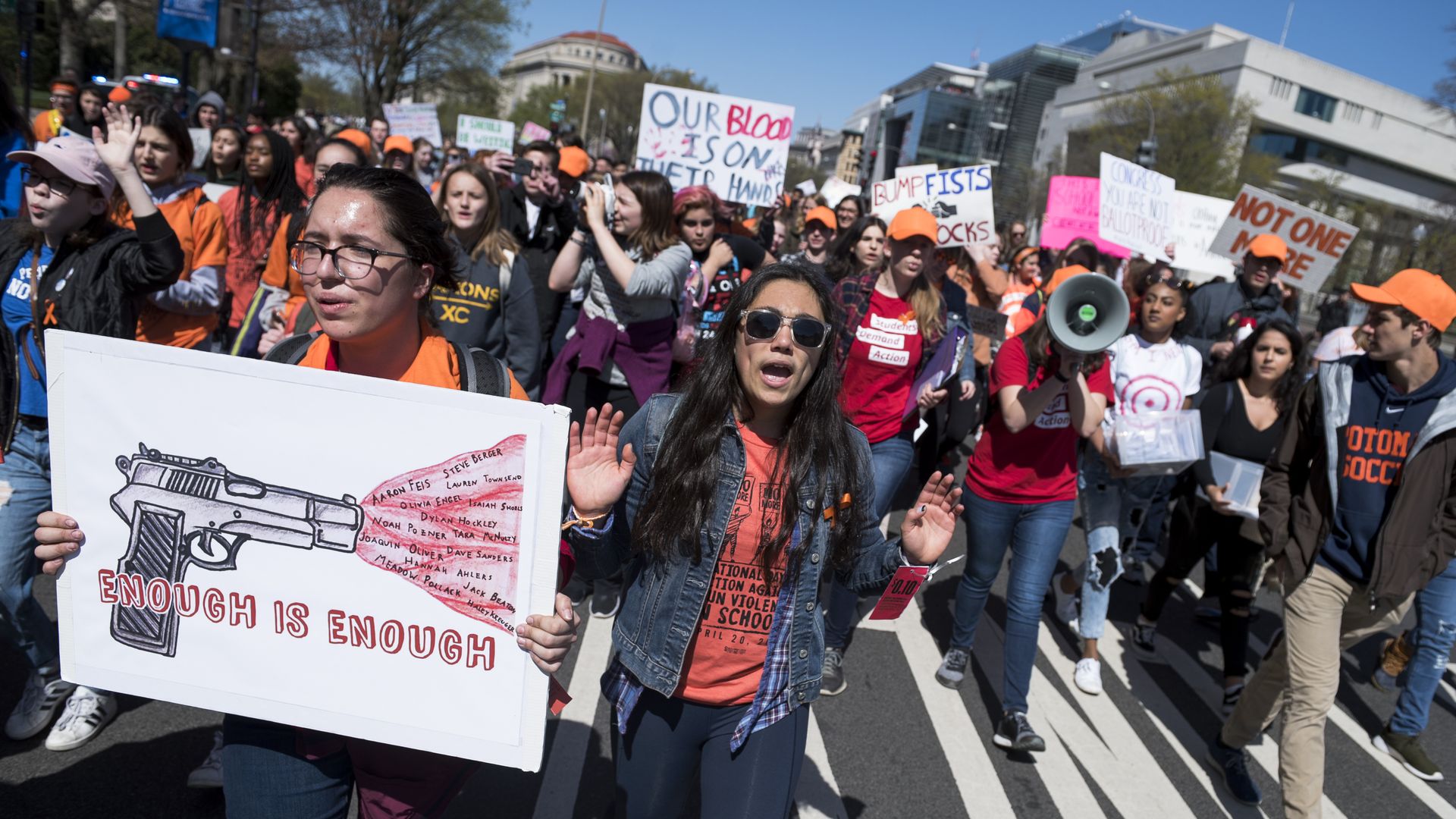 Students walk towards the Capitol in D.C. holding signs reading "Enough is enough" with drawings of a gun.