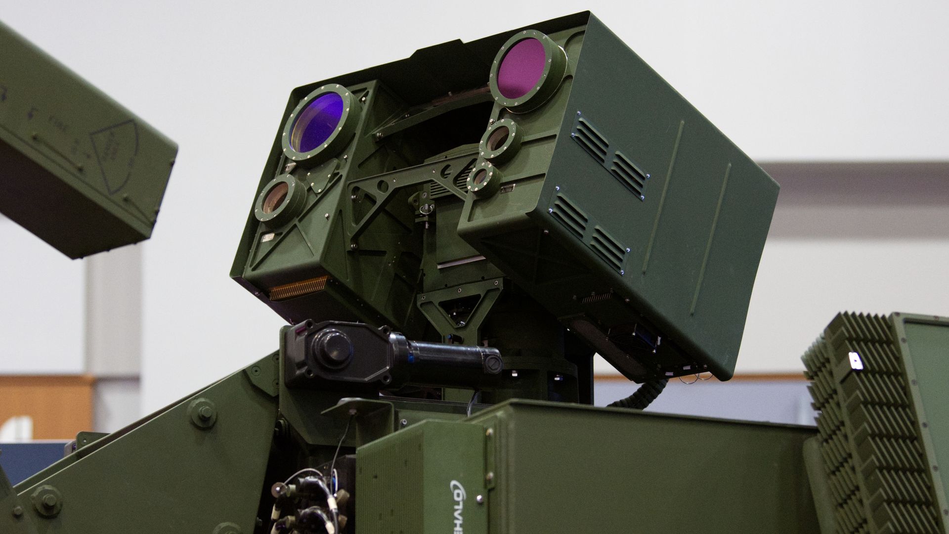 A BlueHalo laser weapon is mounted to a Stryker combat vehicle. It is mostly green. The background is white.