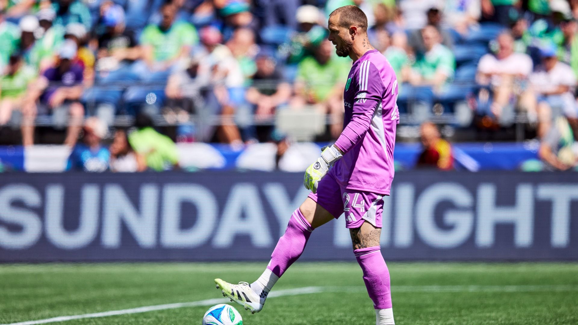 A professional soccer player in a purple uniform stops the ball with his foot. 