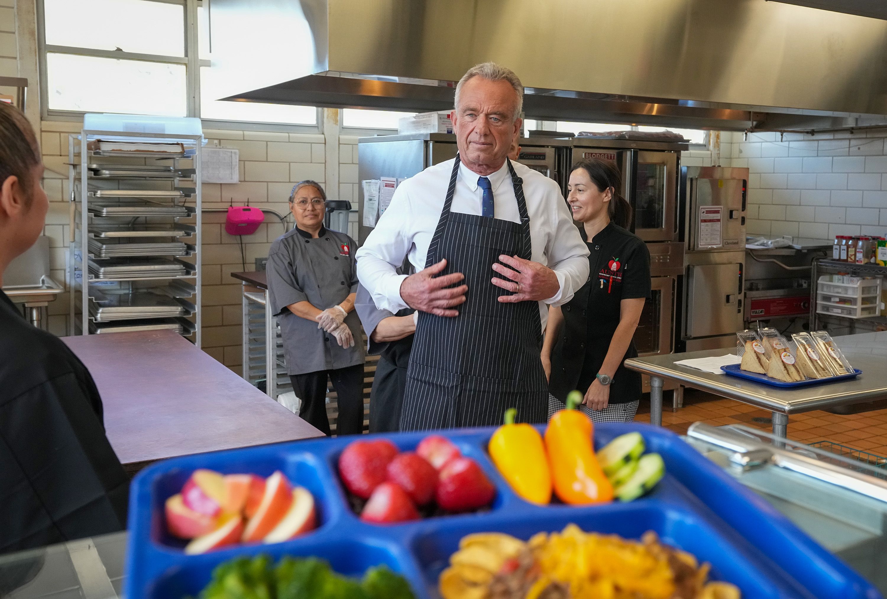 AUSTIN, TEXAS - FEBRUARY 27: U.S. Health and Human Services Secretary Robert F. Kennedy Jr. puts on his apron before helping to serve lunch during a tour of the kitchen at Cunningham Elementary School in Austin on Friday, Feb. 27, 2026. Kennedy visited the campus to discuss federal dietary guideline