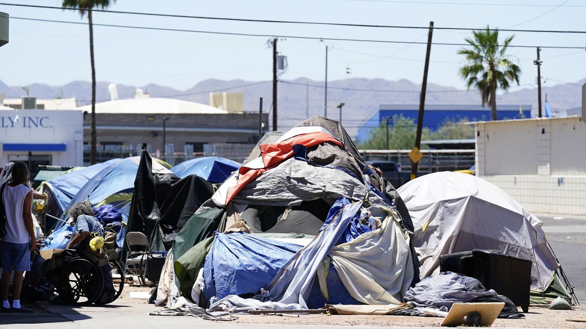 Several tents from a homeless encampment sit clustered along a sidewalk. 