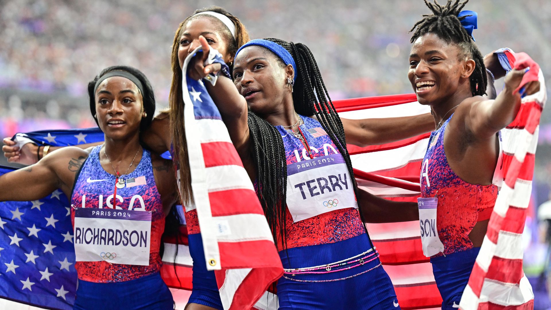 Four Team USA track and field women athletes standing with the American flag.