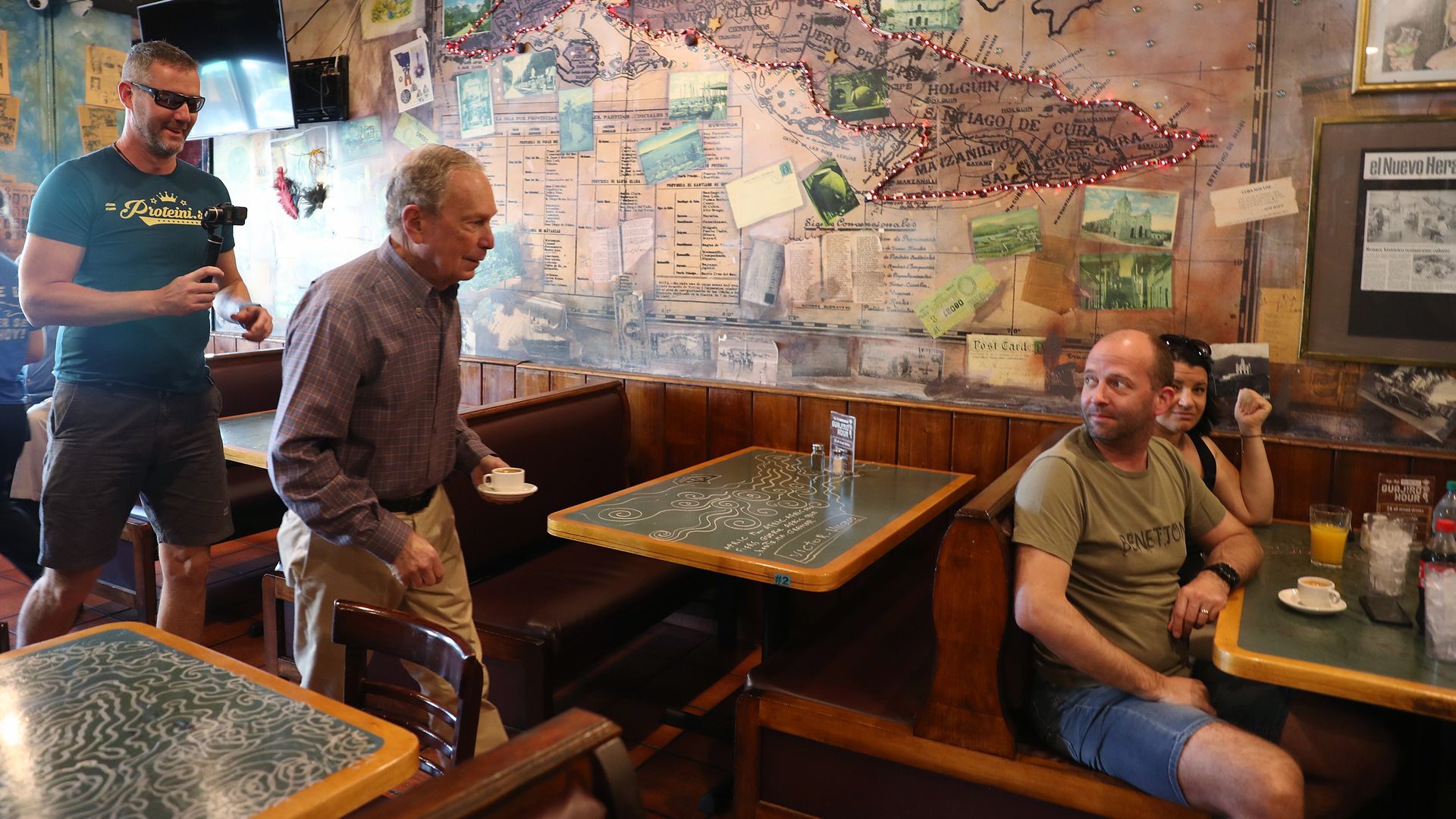Mike Bloomberg holds a cup of coffee as he walks through Cuban restaurant in Florida