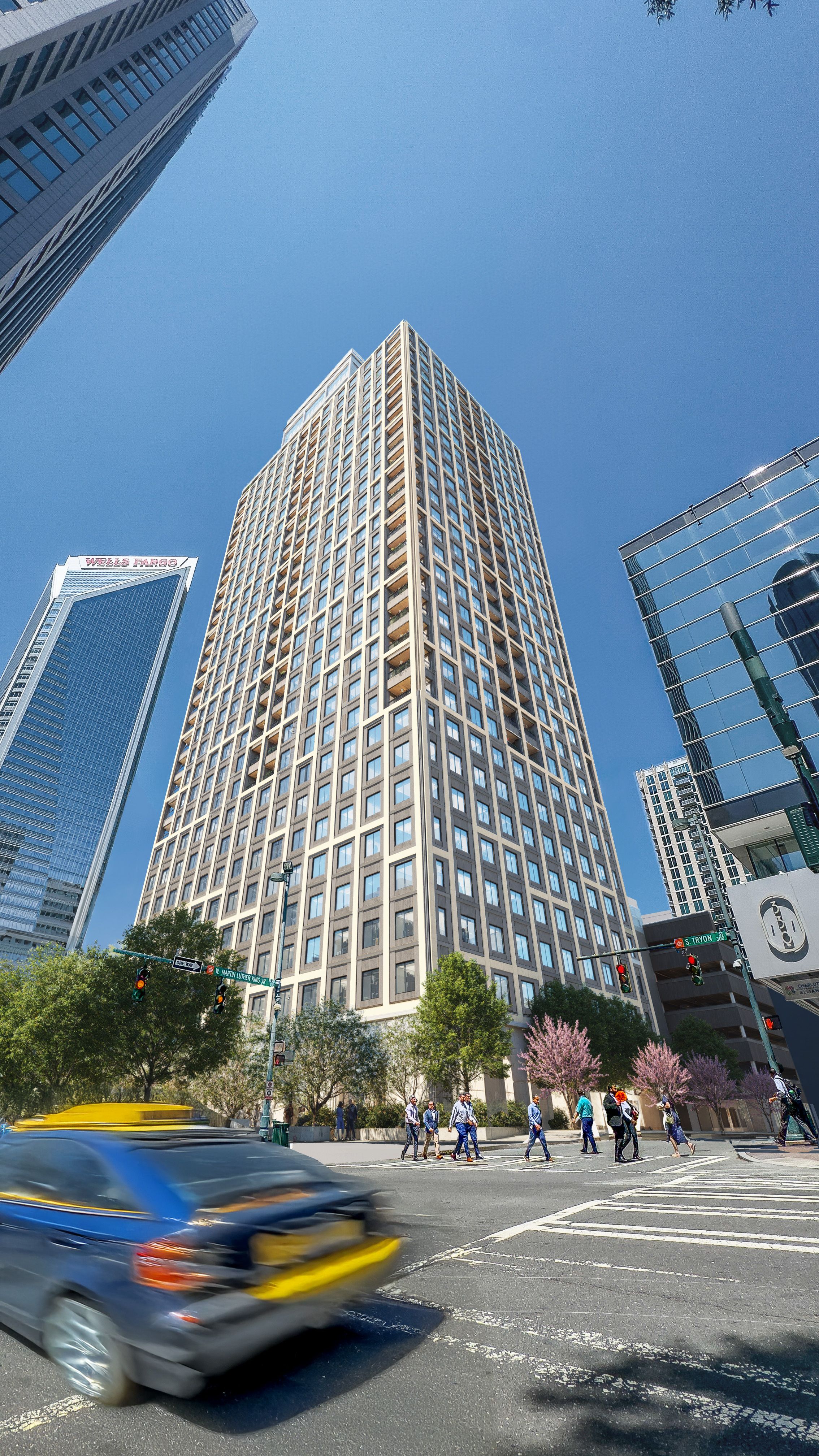 A tall beige skyscraper centers the frame, flanked by glass towers under a clear blue sky. Pedestrians cross the street as a yellow taxi blurs past; pink blossoms line the sidewalk.