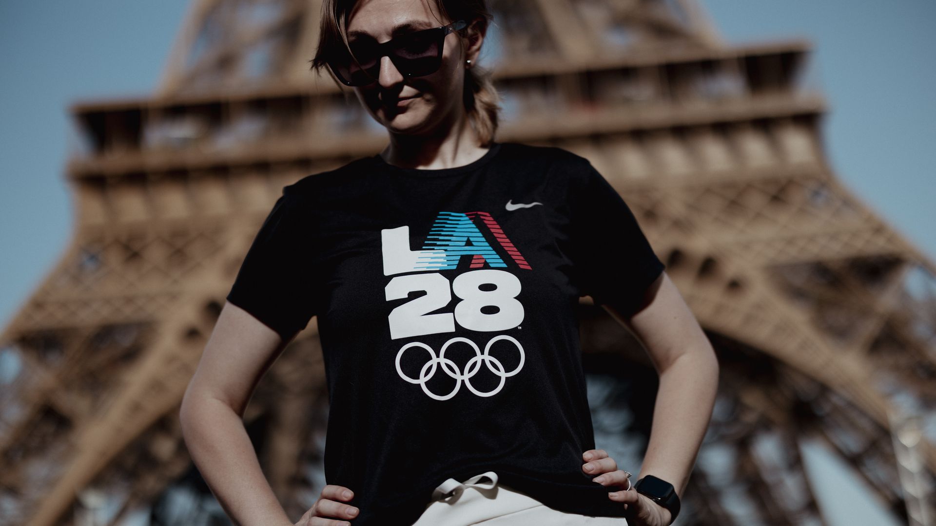 A woman wearing an LA28 shirt in front of the Eiffel Tower