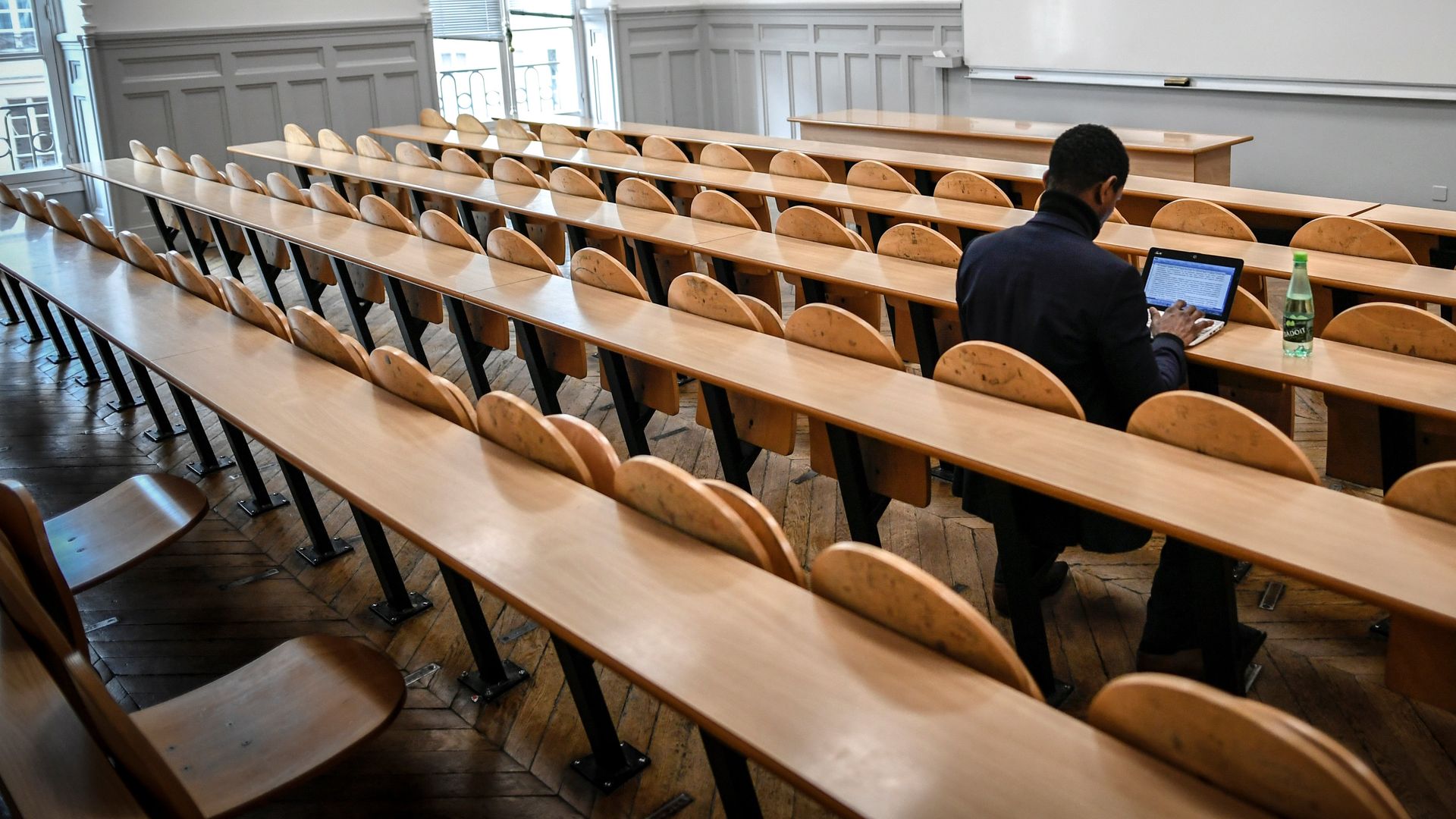 A student sits in an empty classroom, facing a whiteboard