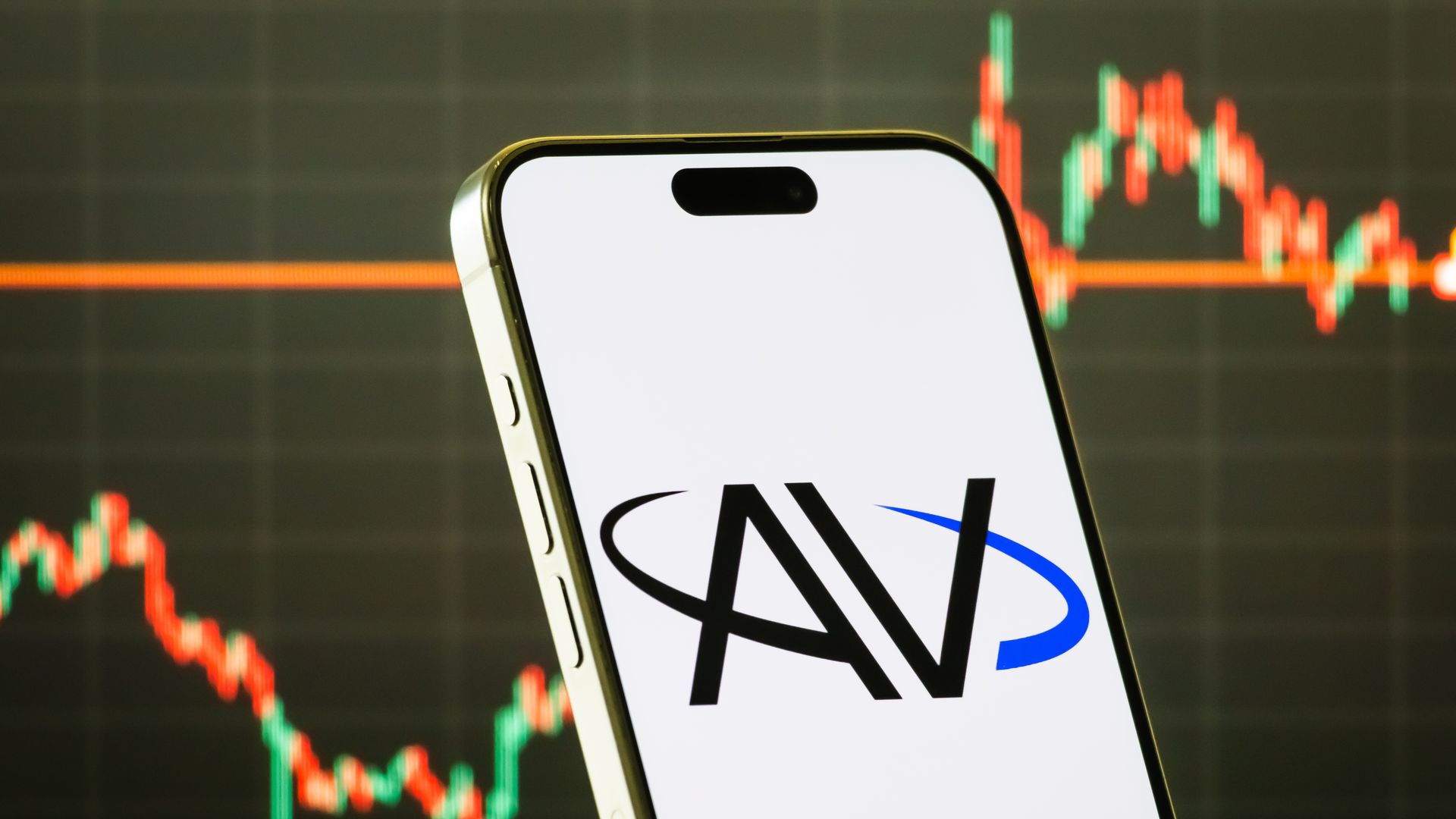 Close-up of a tilted smartphone with a white screen showing the black NAV logo and a blue swoosh; blurred red and green candlestick stock chart in the dark background.
