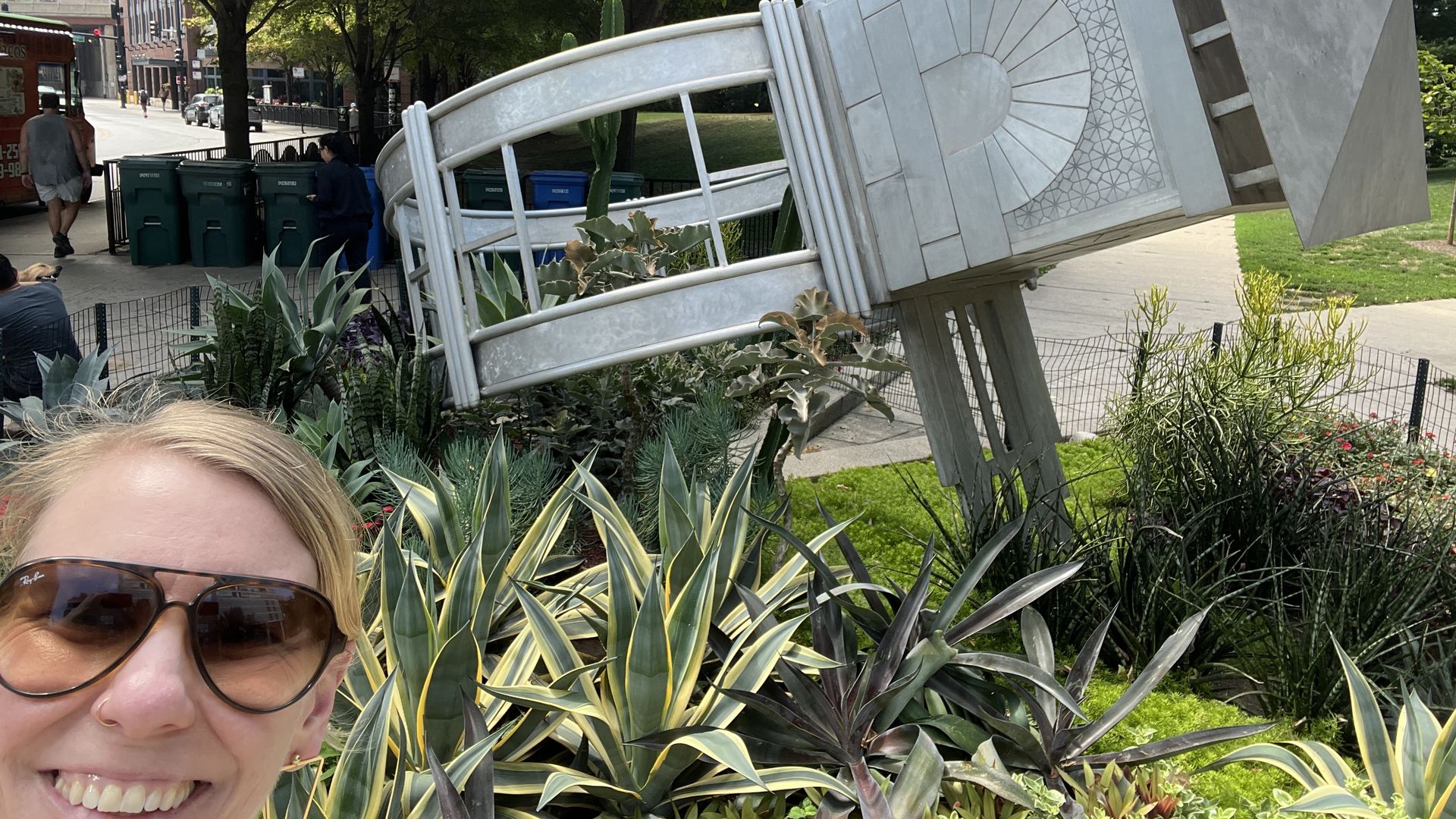 The face of a woman standing in front of a stainless steel sculpture.