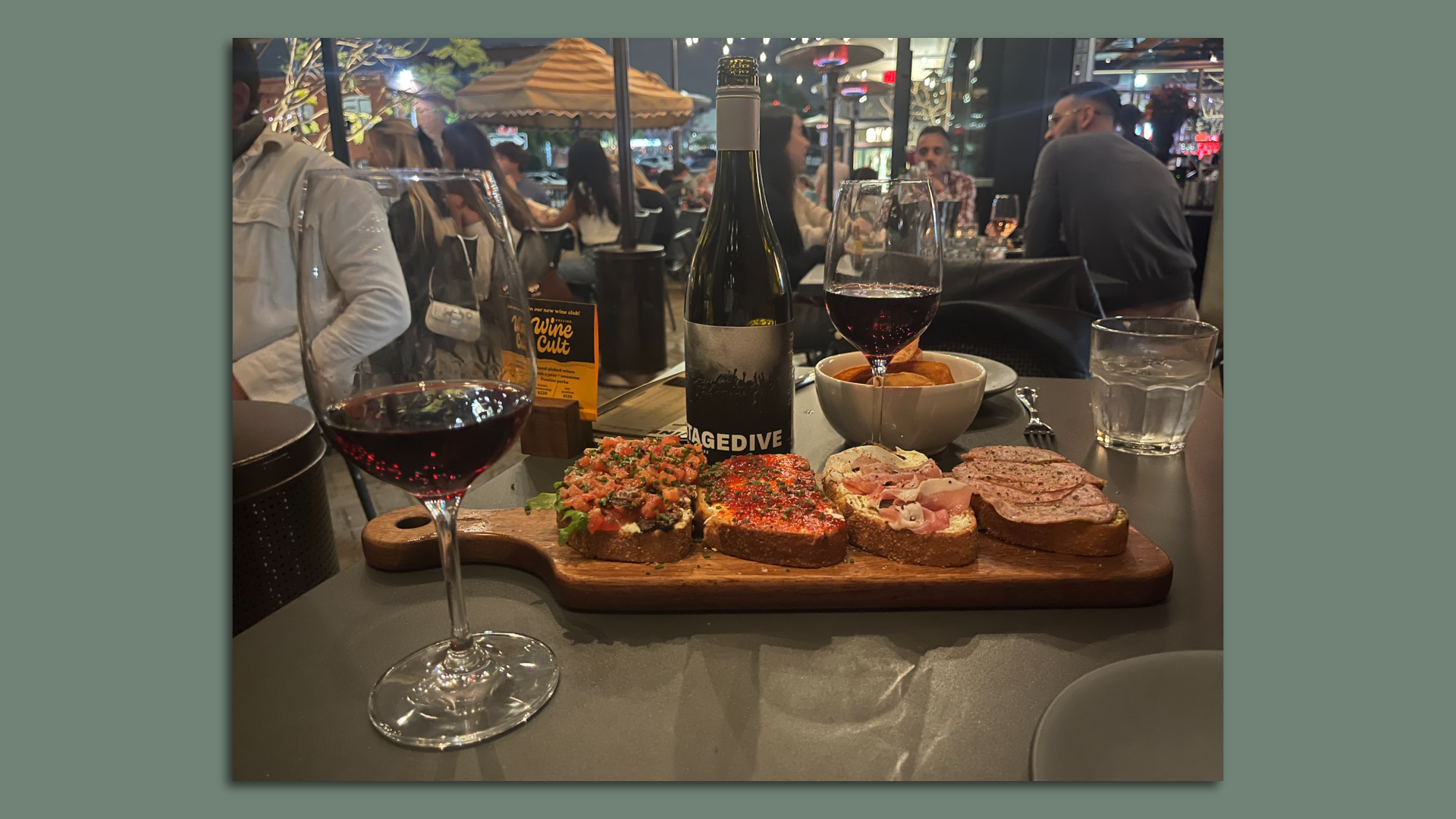 A bottle of wine, two glasses of wine and a board of bruschetta on a patio table.