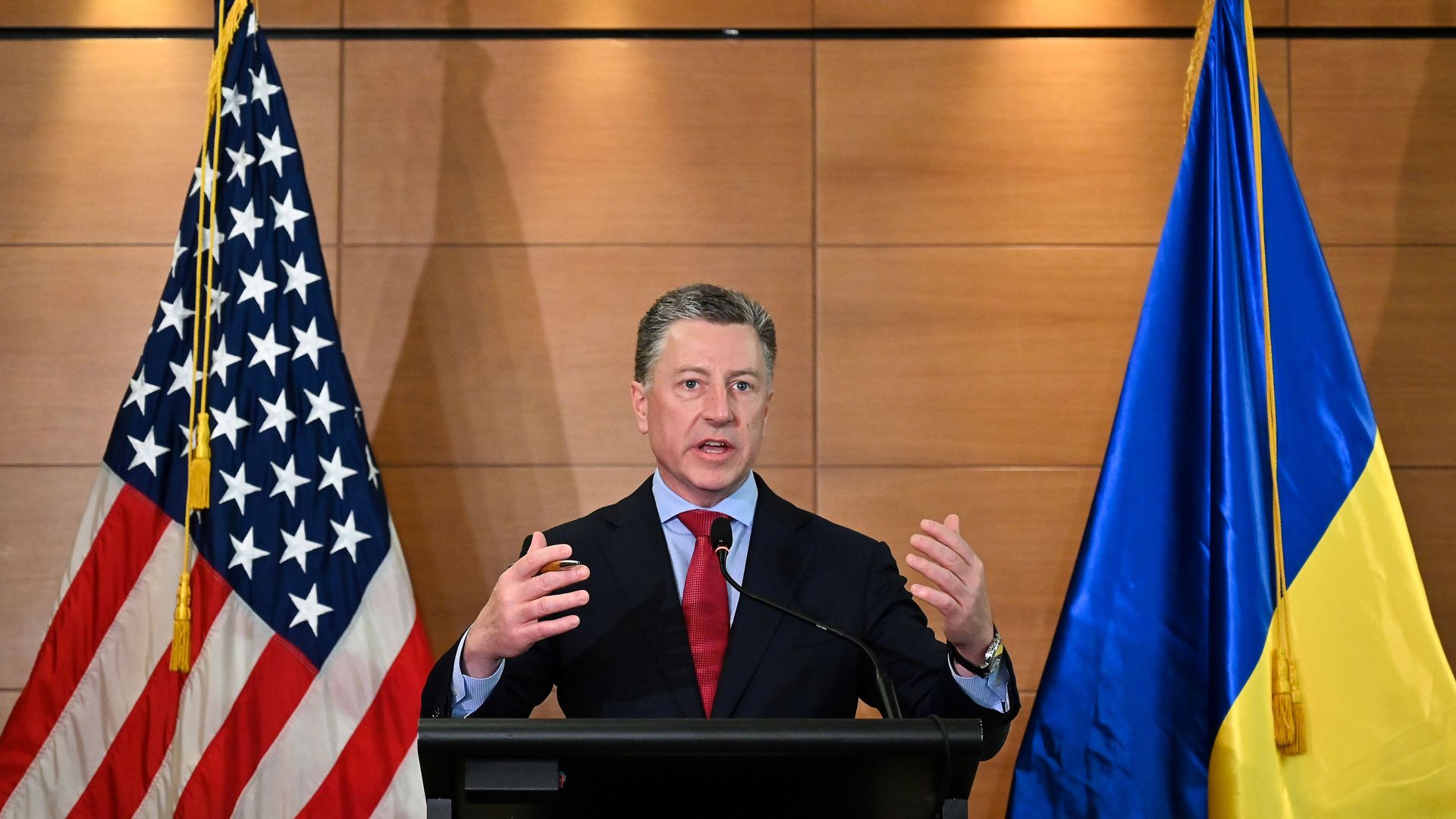 In this image, Kurt speaks at a podium between two flags.