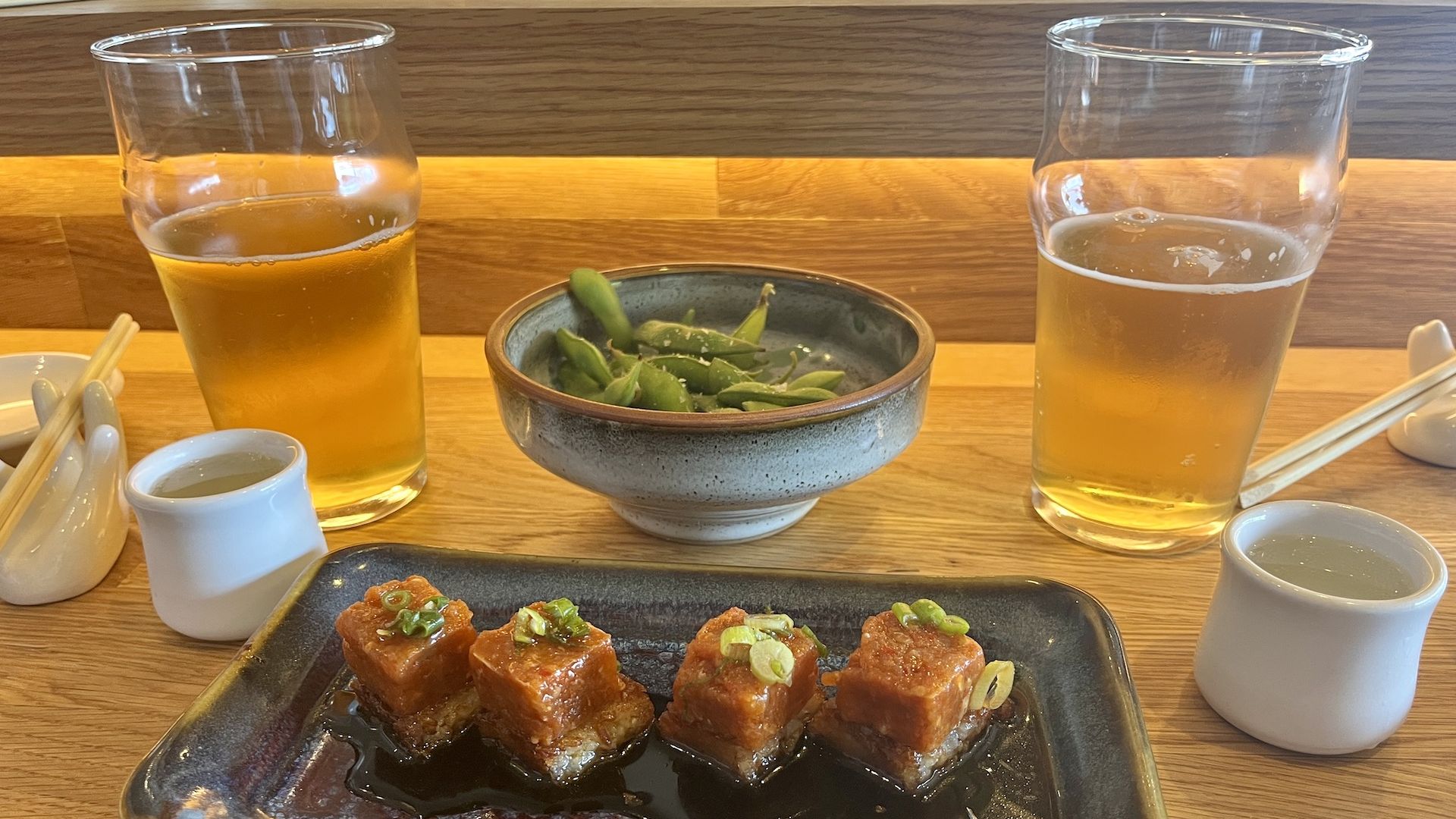 A spicy tuna crispy rice dish, sake, beer and edamame at a table.