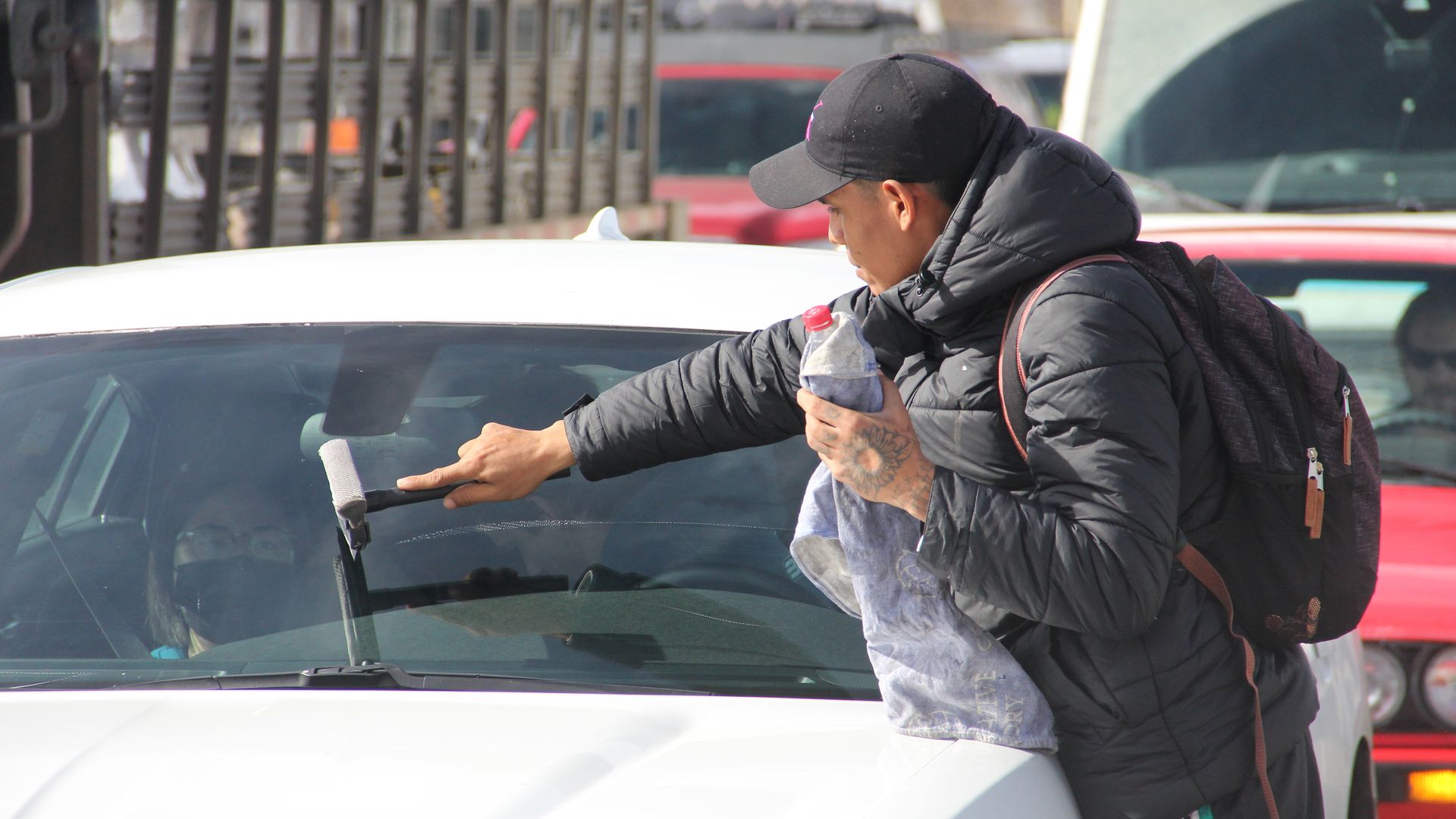 A Venezuelan migrant cleans a car windshield near a busy intersection in Denver.