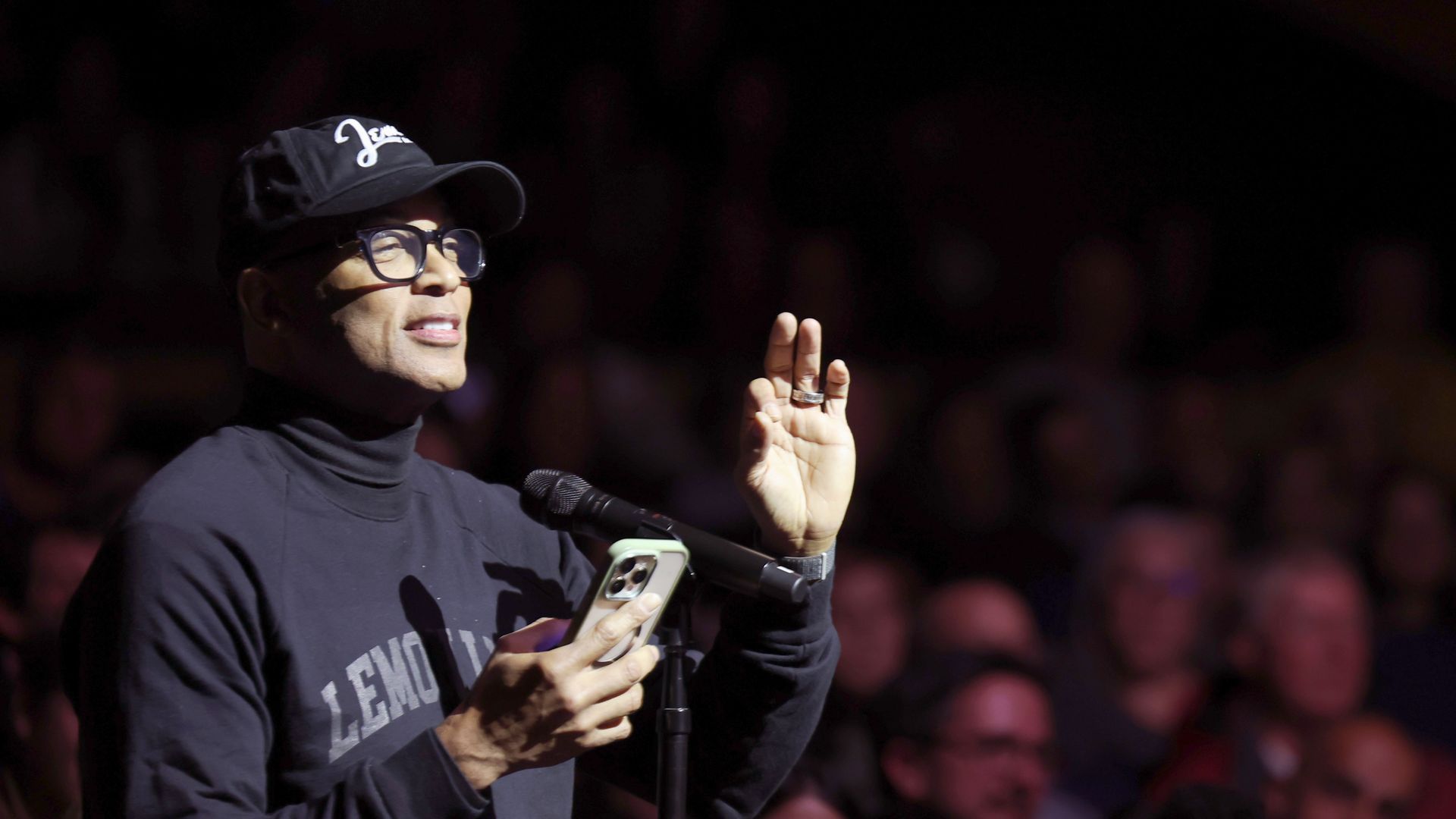 Don Lemon holds a phone while speaking into a microphone 