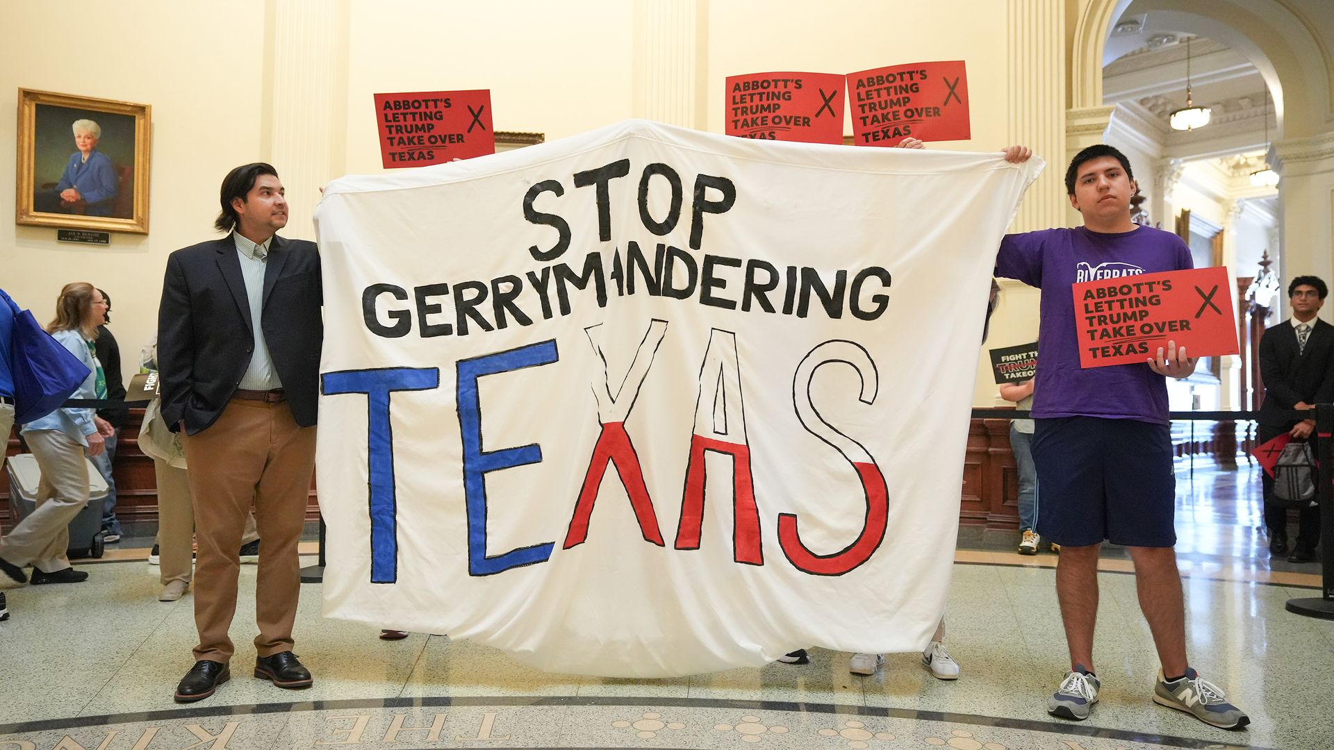 Two men hold up a large white sign that reads "Stop Gerrymandering Texas" while protesting redistricting plans at the Texas Capitol in Austin in August 2025. The word "Texas" is colored in red, white and blue. 
