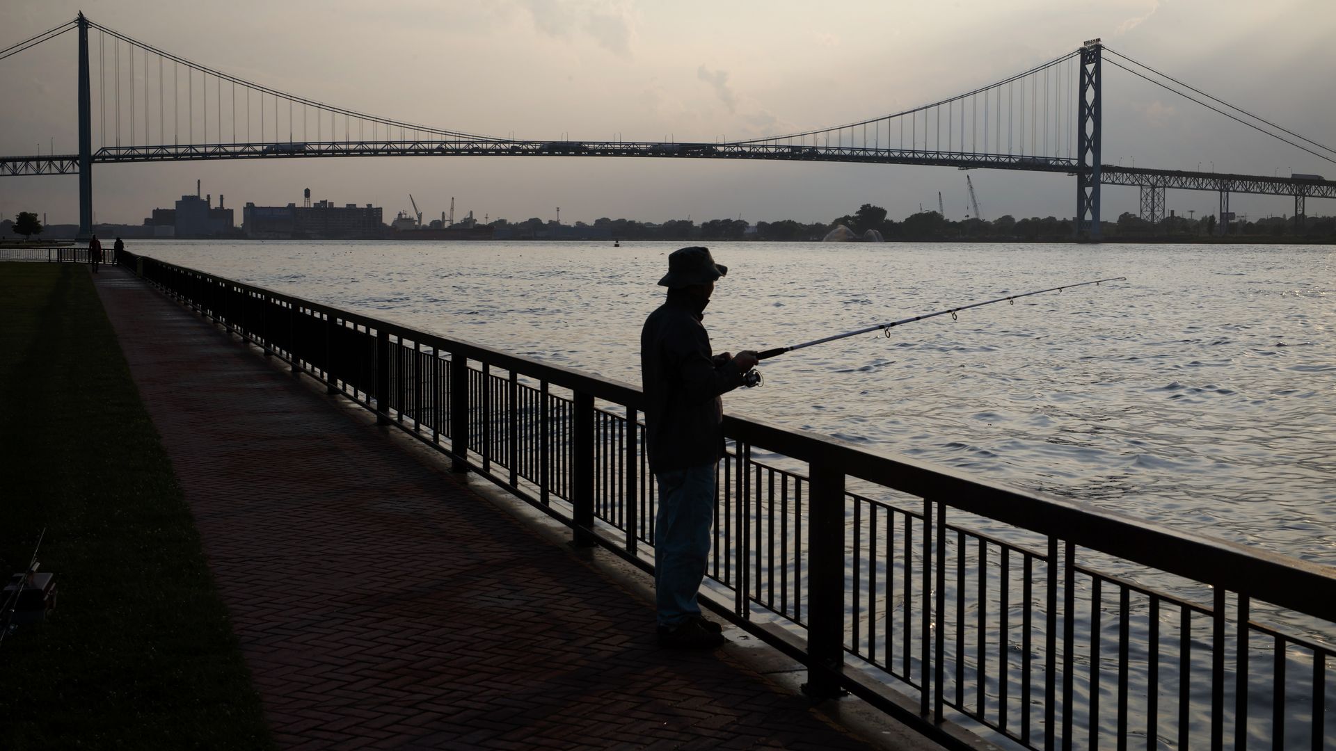 A person fishing by the Detroit River with the Ambassador Bridge in the background