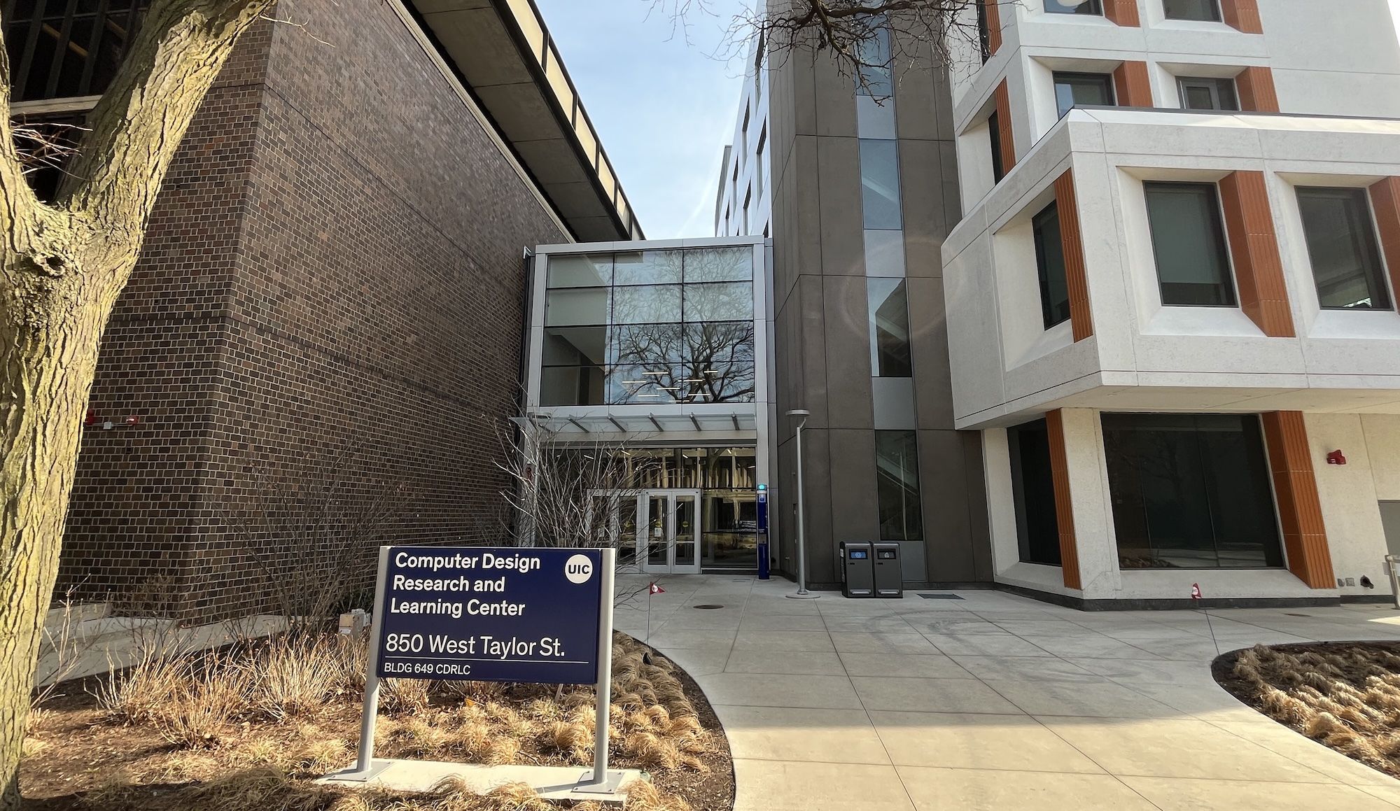 Modern campus building with a brick left wall, glass entry canopy, and a light gray/white facade with orange accents; a blue UIC sign reads "Computer Design Research and Learning Center, 850 West Taylor St."