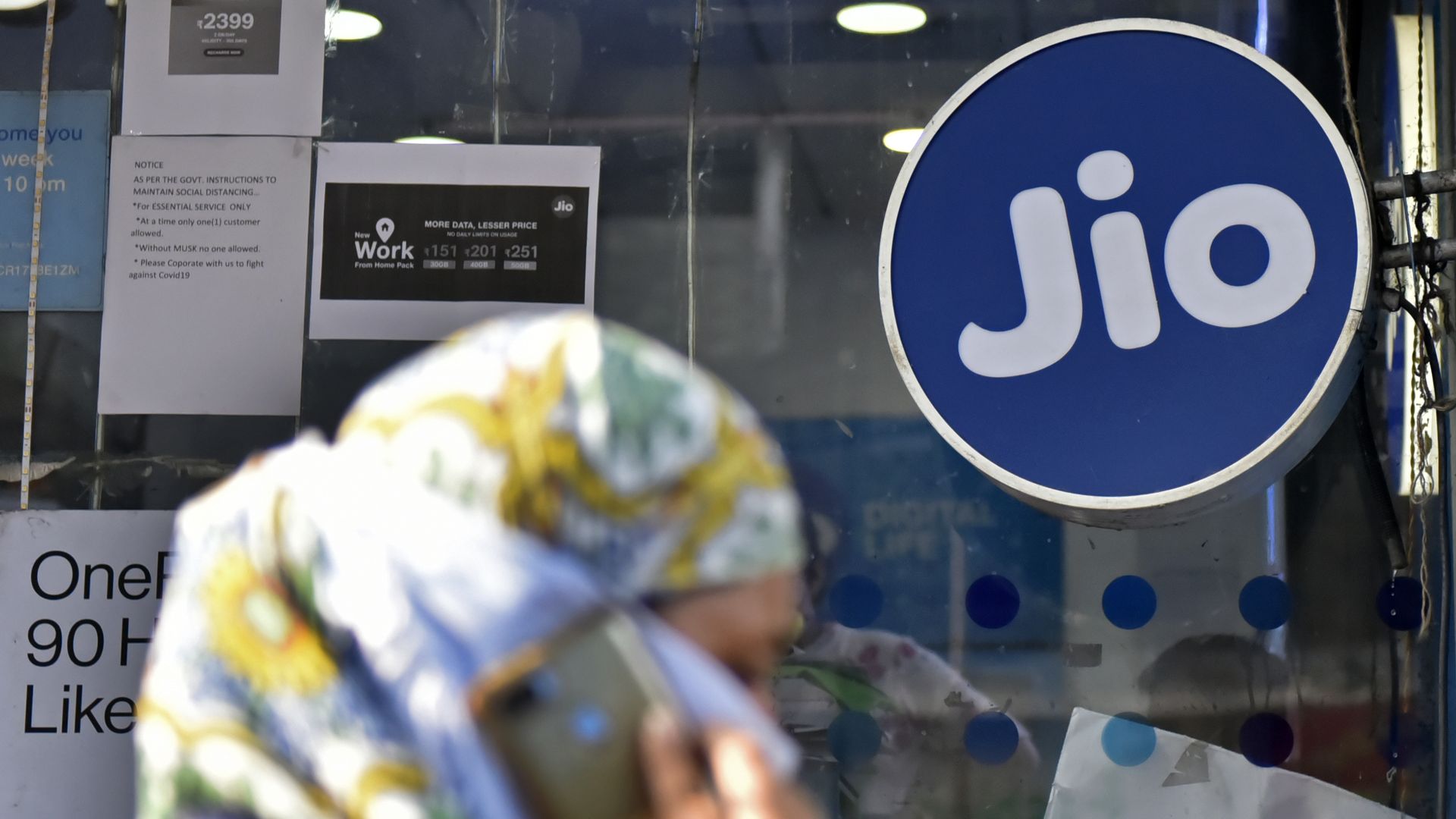 A woman talking on a cellular phone walks past a Jio store in Kolkata, India.