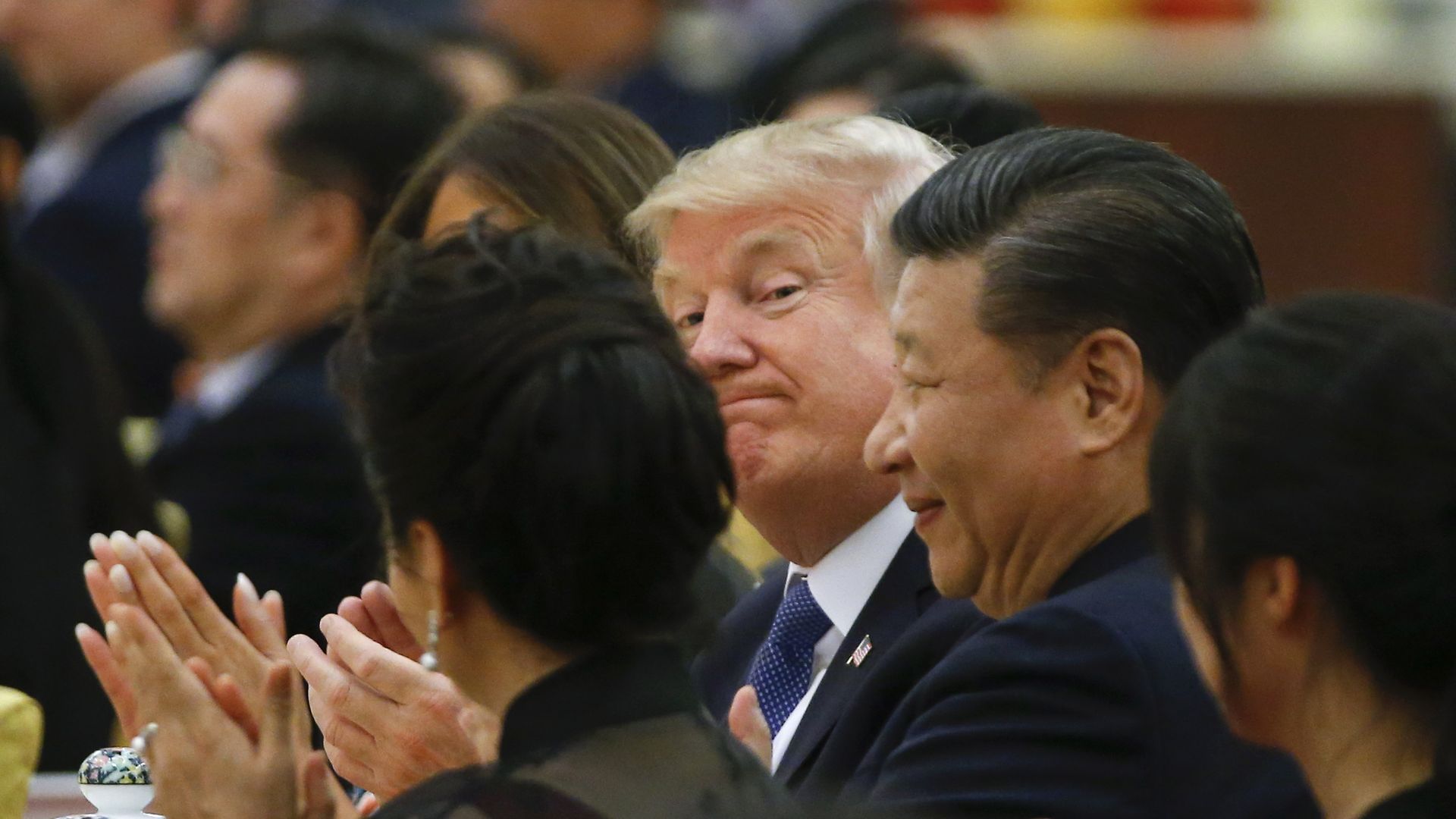 Photo of President Trump smirking at camera as he sits next to President Xi at a function