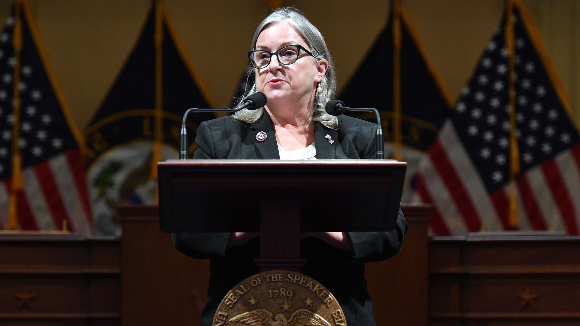 Rep. Susan Wild speaks at a podium wearing a gray suit, white shirt and glasses.