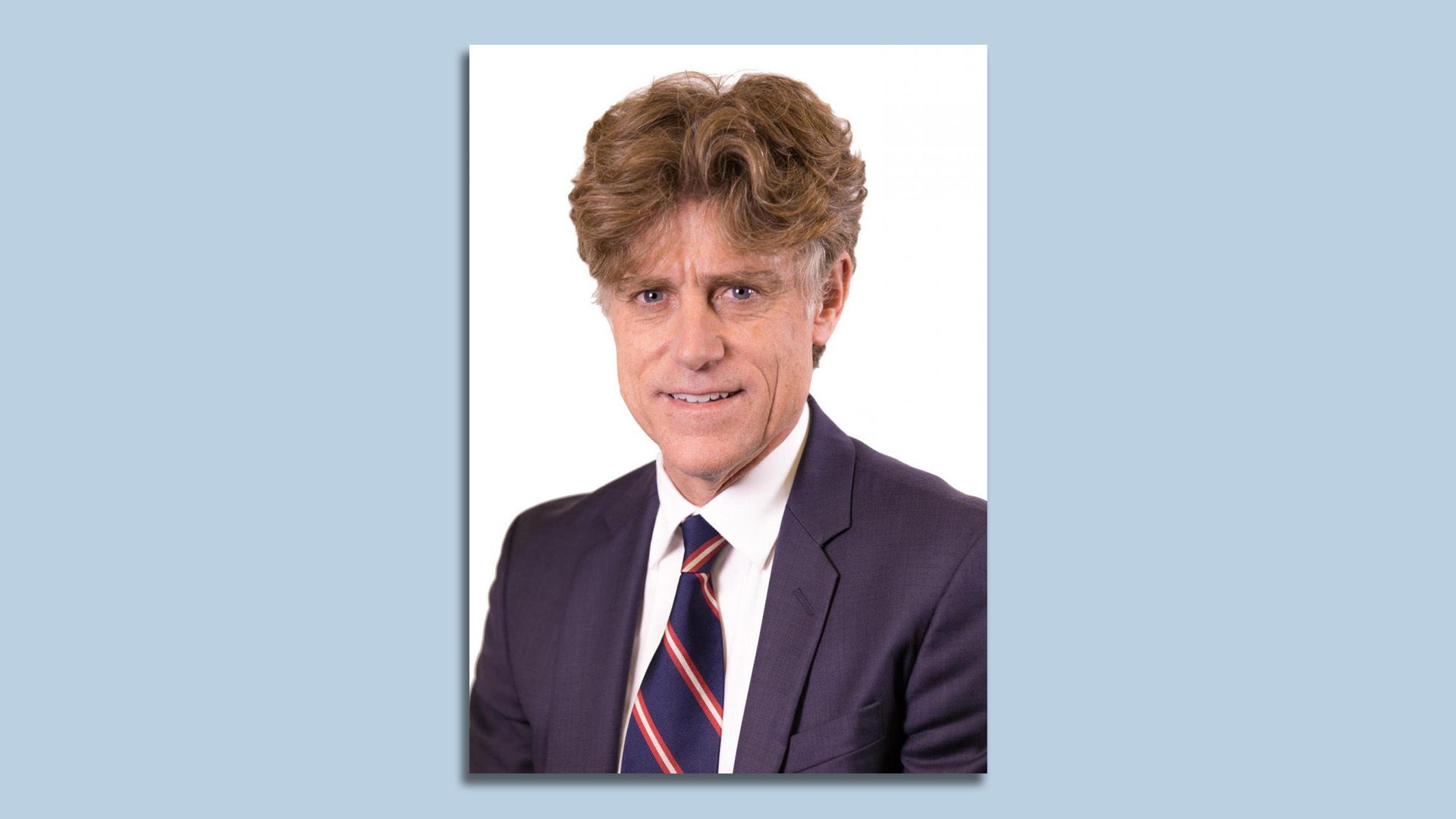 A headshot of Tim Keane wearing a suit and tie on a white background